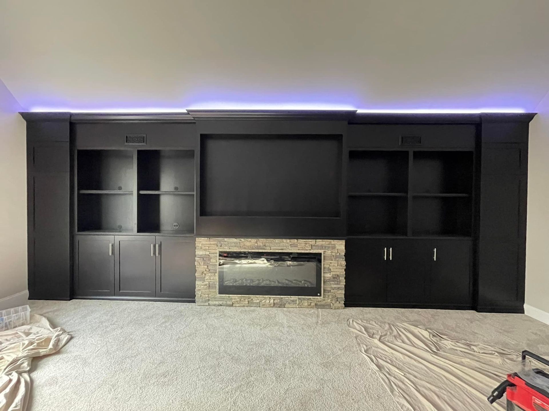 Black entertainment center with built-in fireplace, shelves, and cabinets. Ambient purple light along the top.