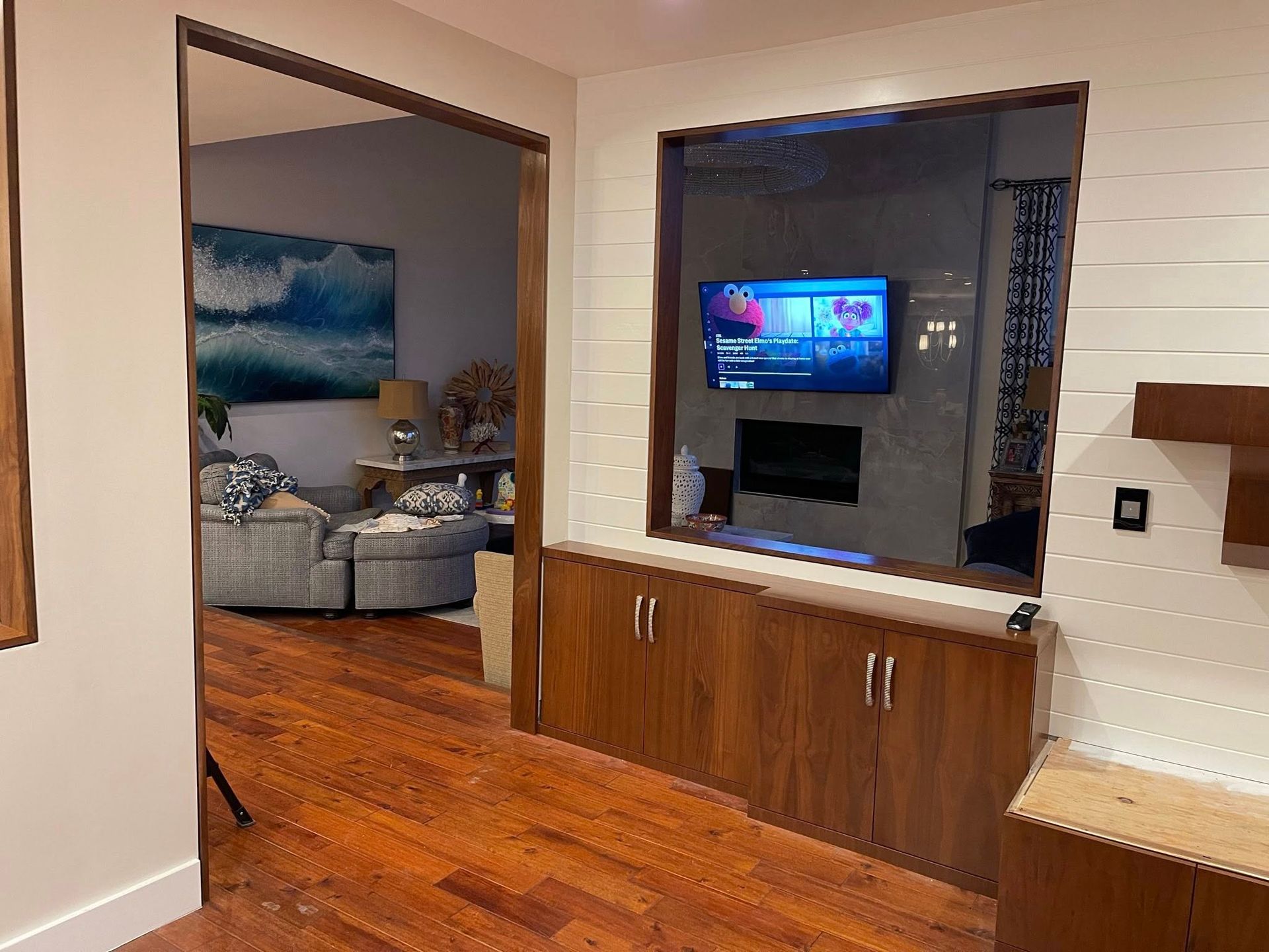 Living room with TV above a fireplace, visible through a doorway. Wooden cabinets and flooring.