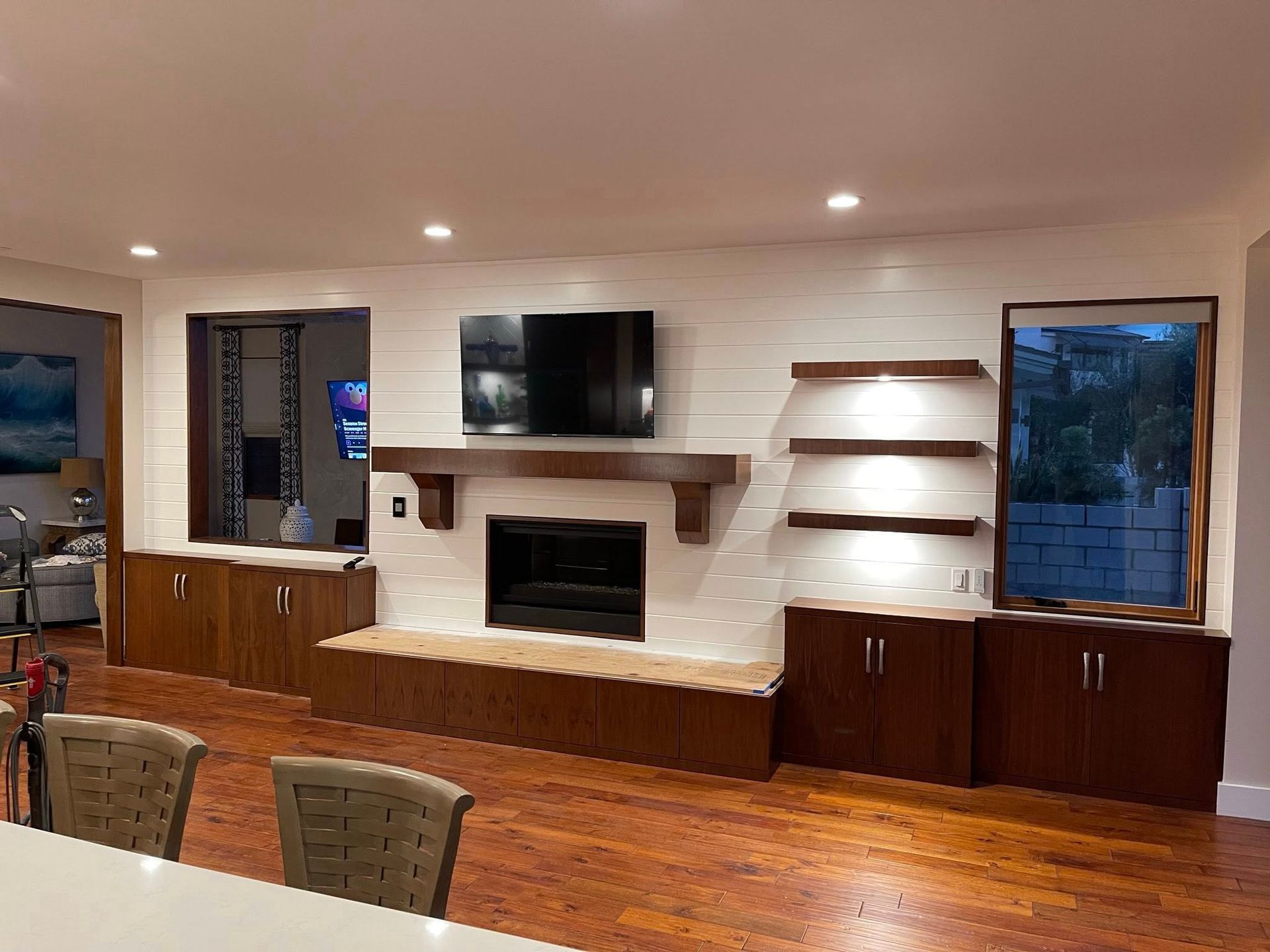 Living room with fireplace, TV, and built-in wooden cabinets. White brick wall, wooden shelves, and hardwood floors.