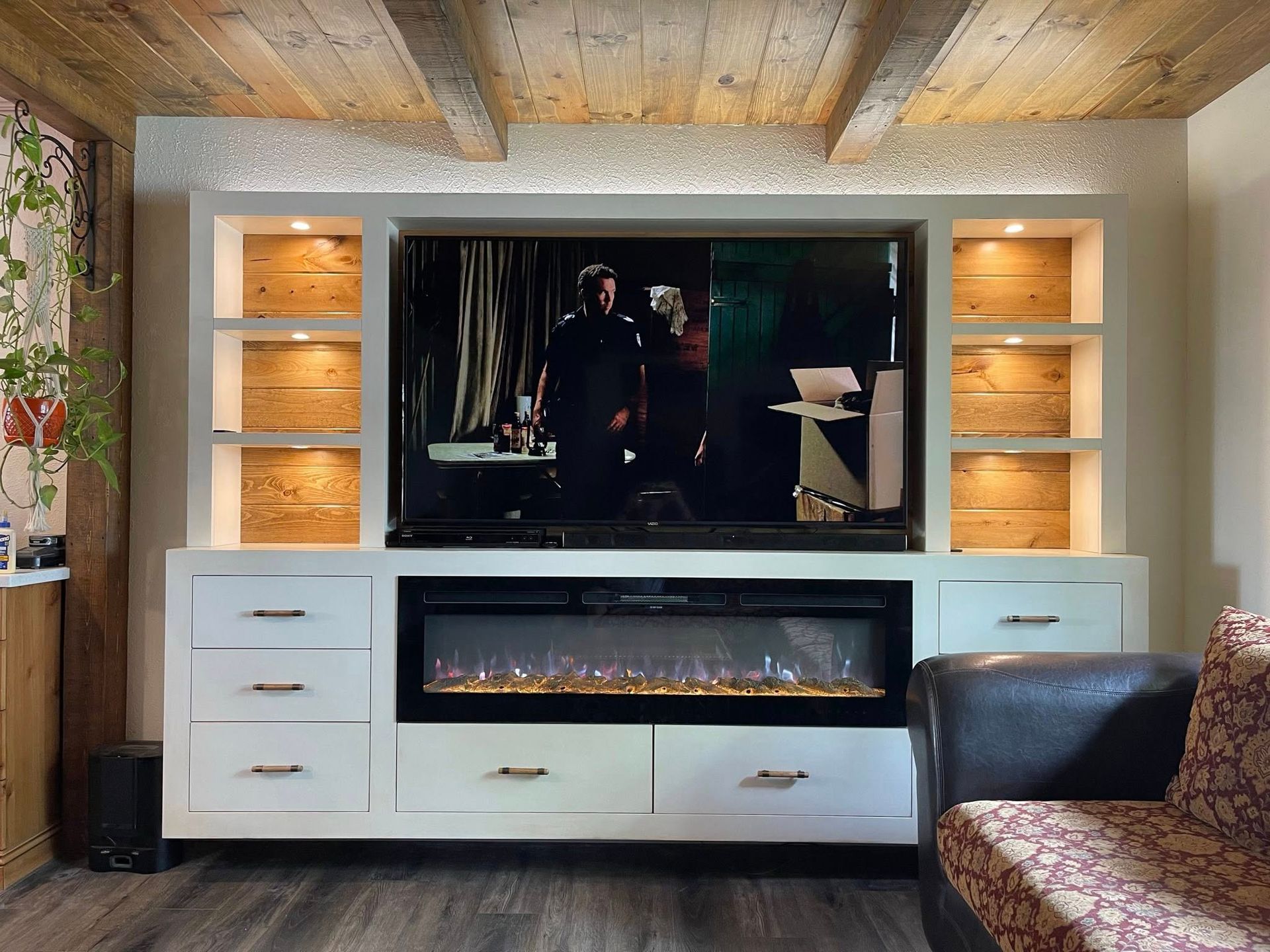 White entertainment center with TV, fireplace, shelves with wood backing, and a couch.