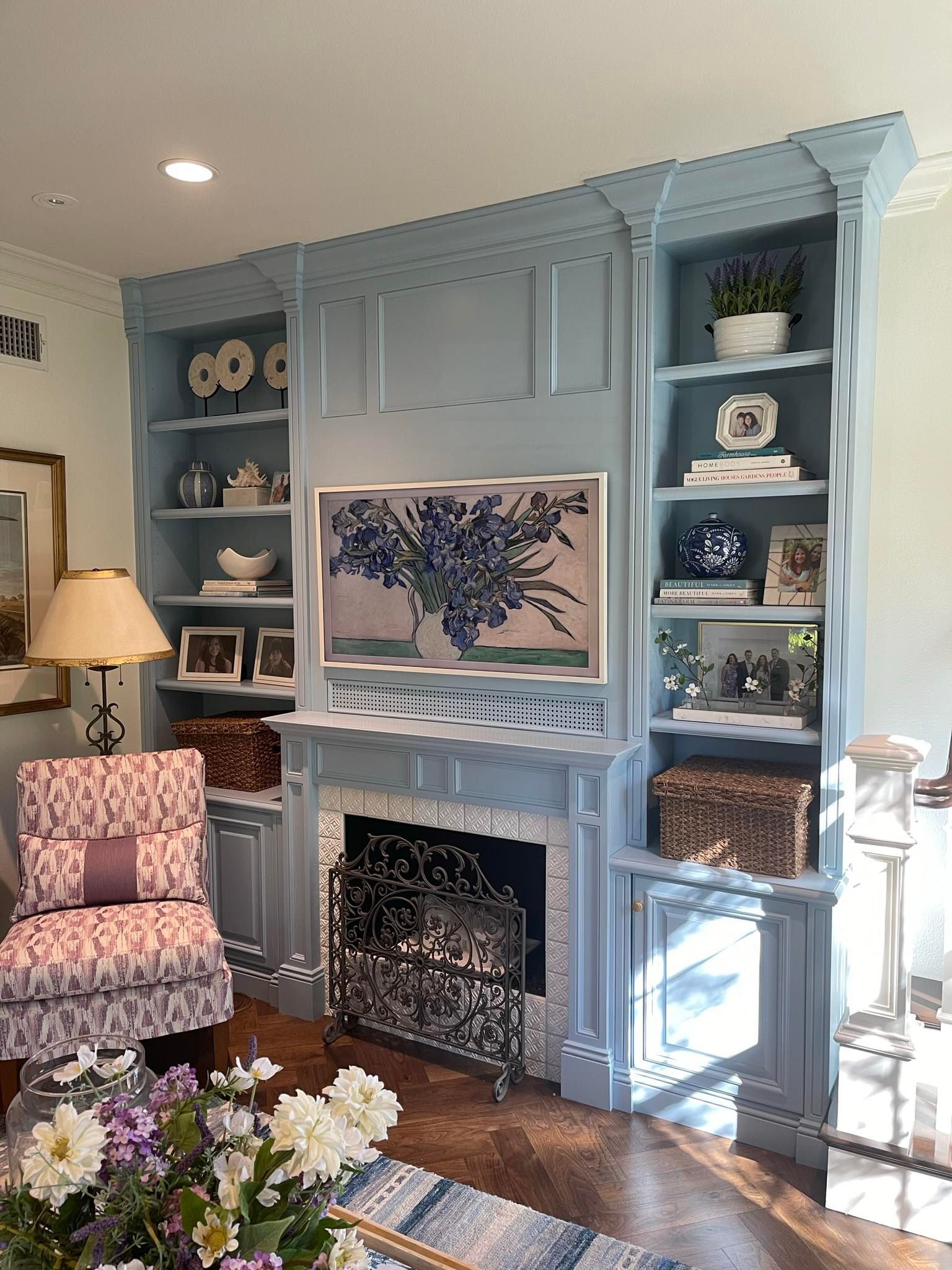 Blue painted built-in shelves with a fireplace and framed artwork, decorated with decor and a patterned chair.