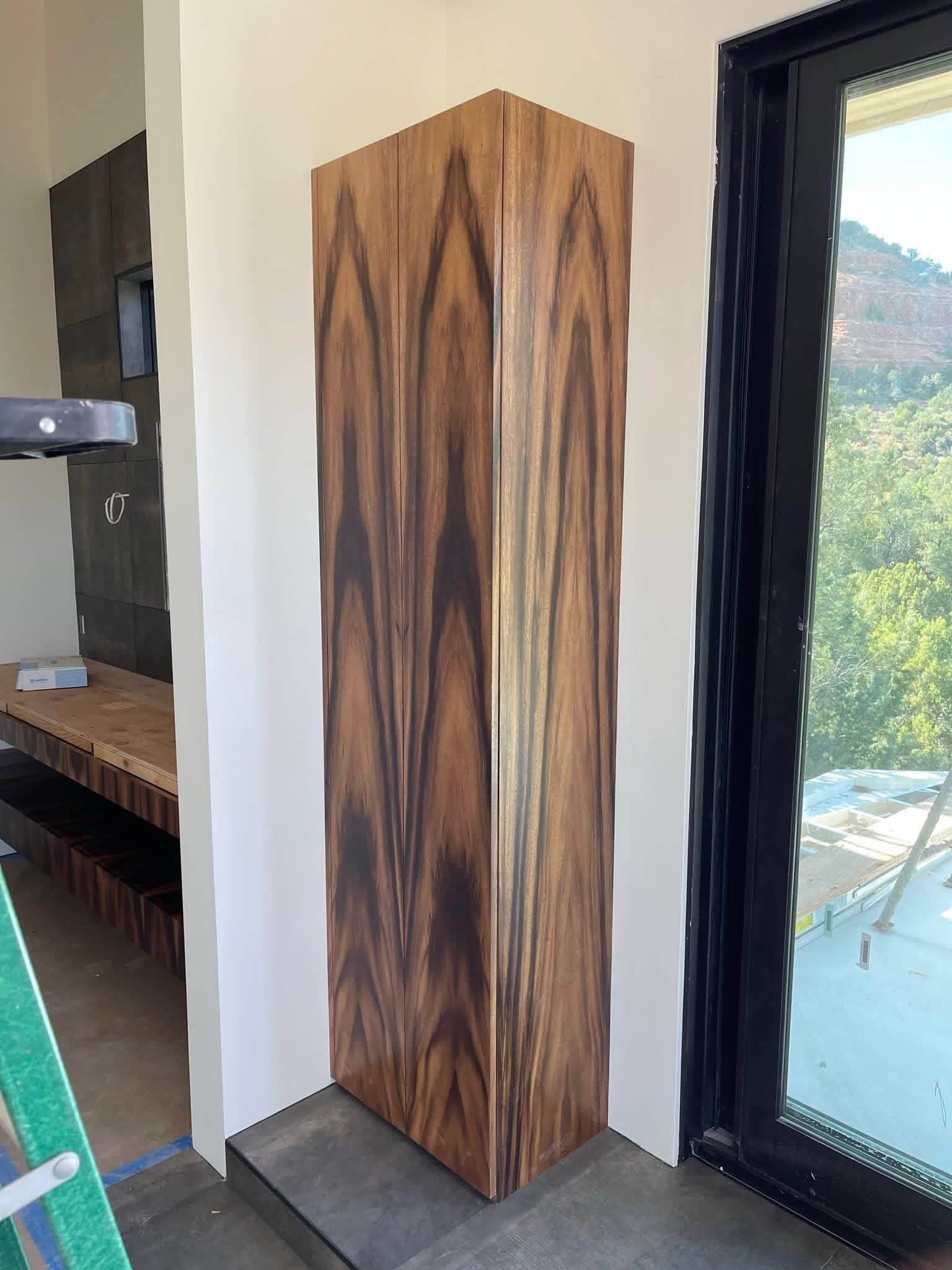 Tall wooden column with dark grain pattern in corner of a building near a window.