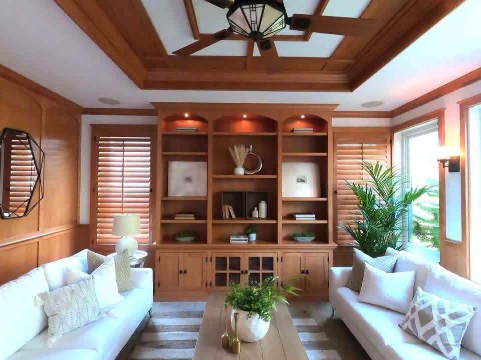 A room with a TV built into a wall, wooden cabinets below, and a glimpse into an adjacent living area.