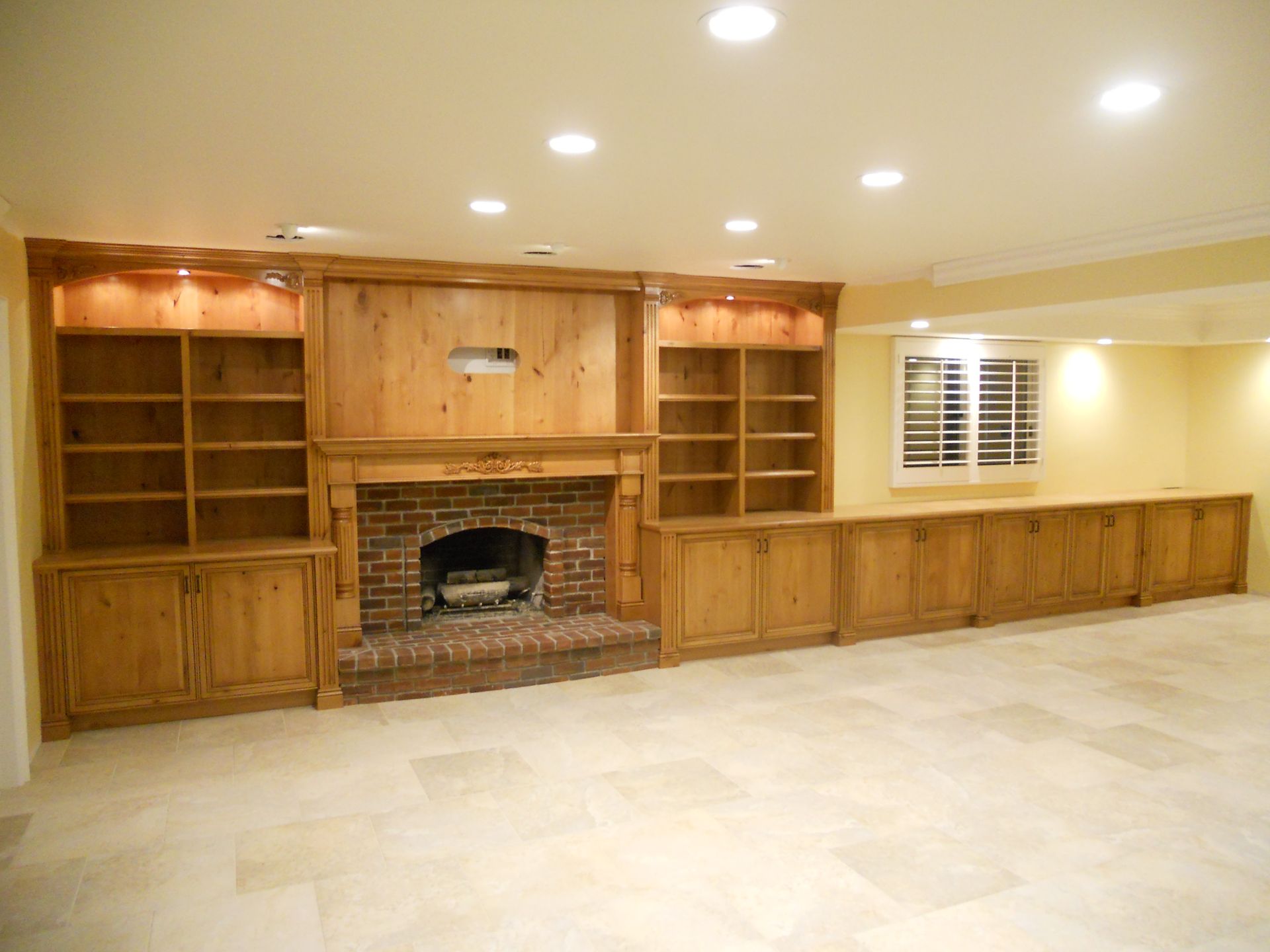 Fireplace with brick surround, built-in wooden bookshelves and cabinets, and a white ceiling with recessed lighting.