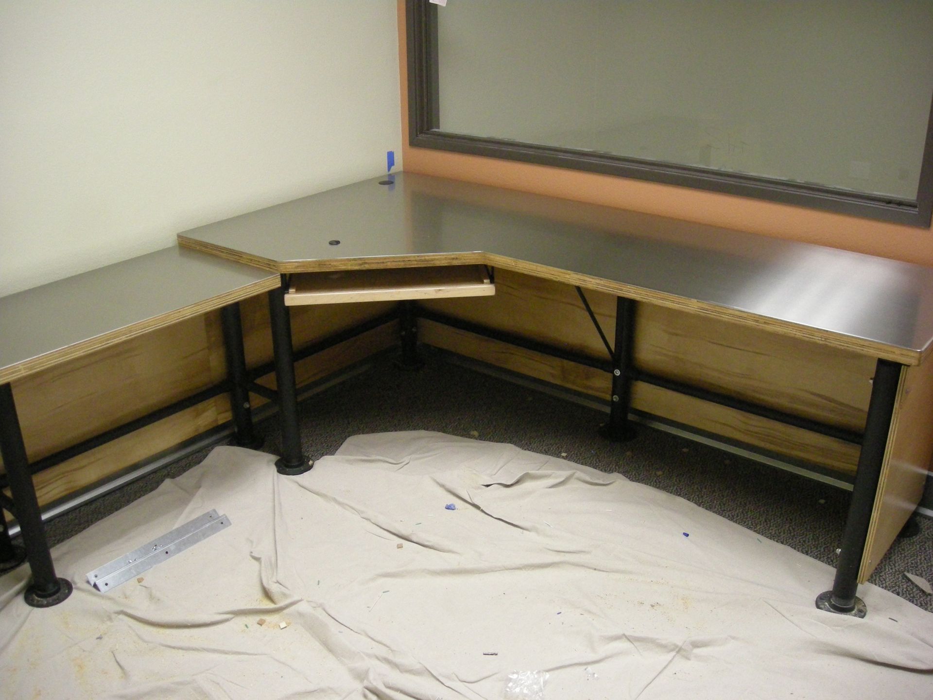 L-shaped desk with a black surface and metal frame, set against a wall with a window.