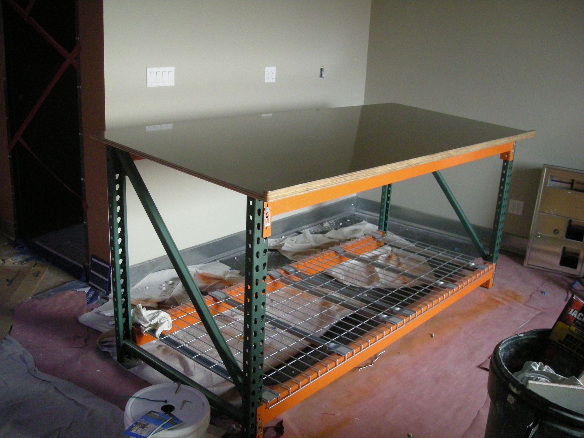 Large metal shelving unit repurposed as a work table, featuring a dark countertop and wire shelving.