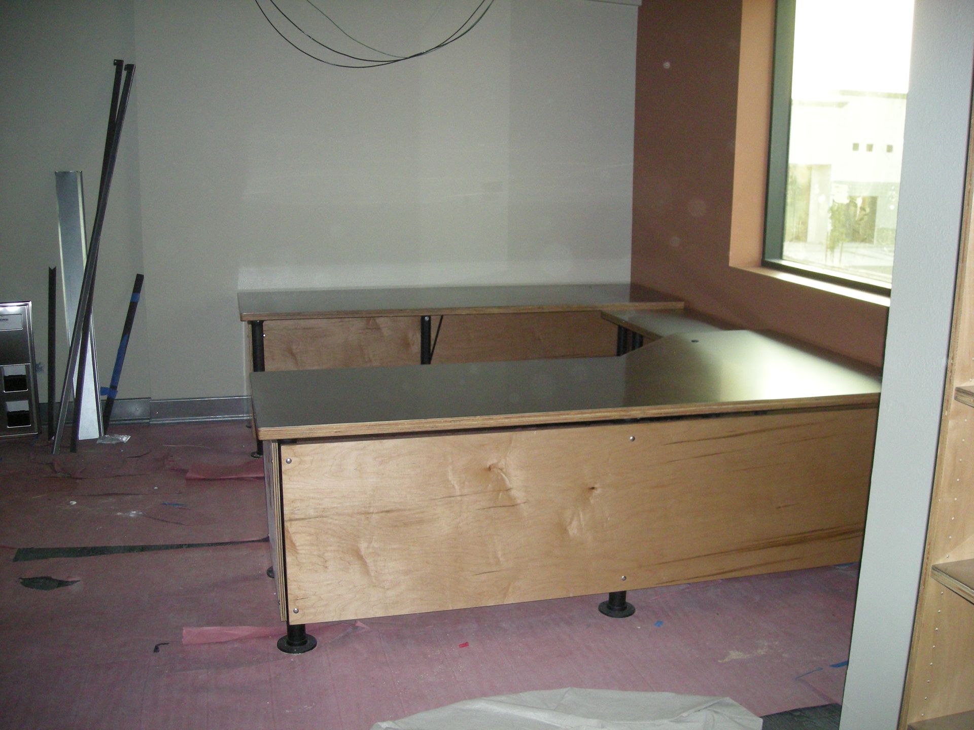 Wooden desk in construction. The desk is L-shaped with exposed wood. Walls are neutral colors.