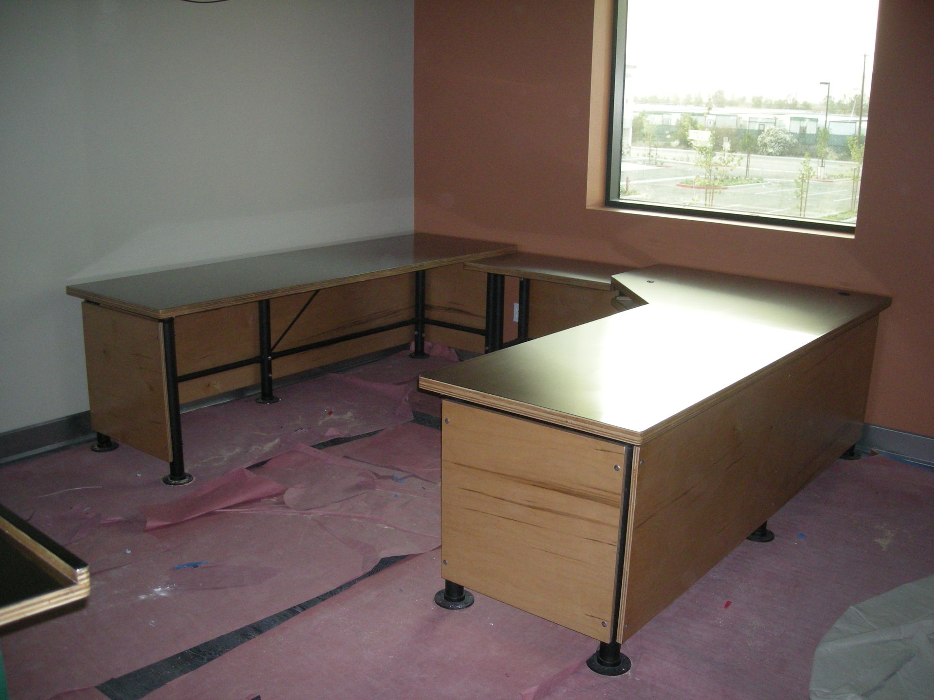A U-shaped office desk with a brown surface and black support beams in an empty room.