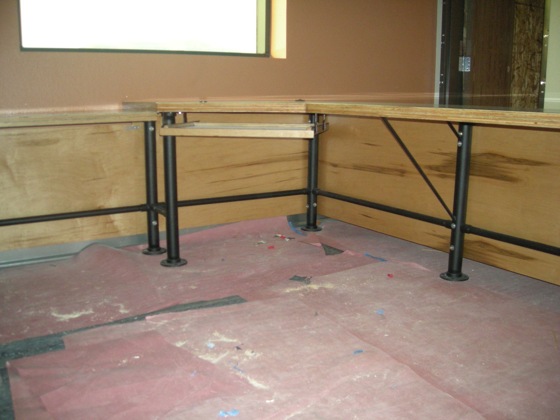 Partially constructed wooden counter with black metal supports in a room under renovation.