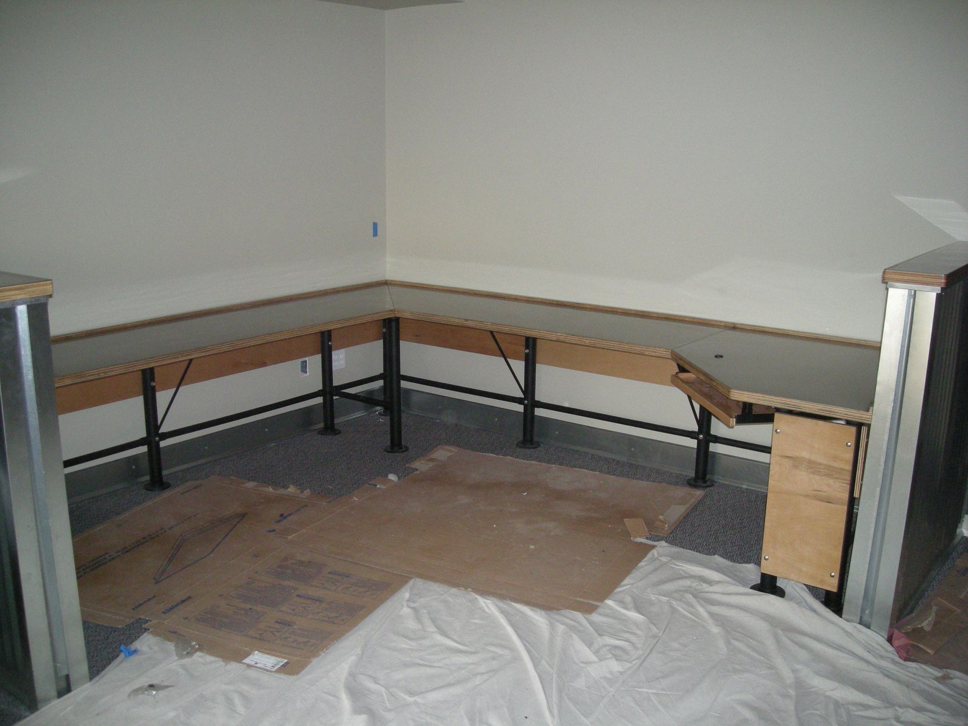 A U-shaped built-in workbench with black metal legs is under construction in a room with white walls and a gray floor.