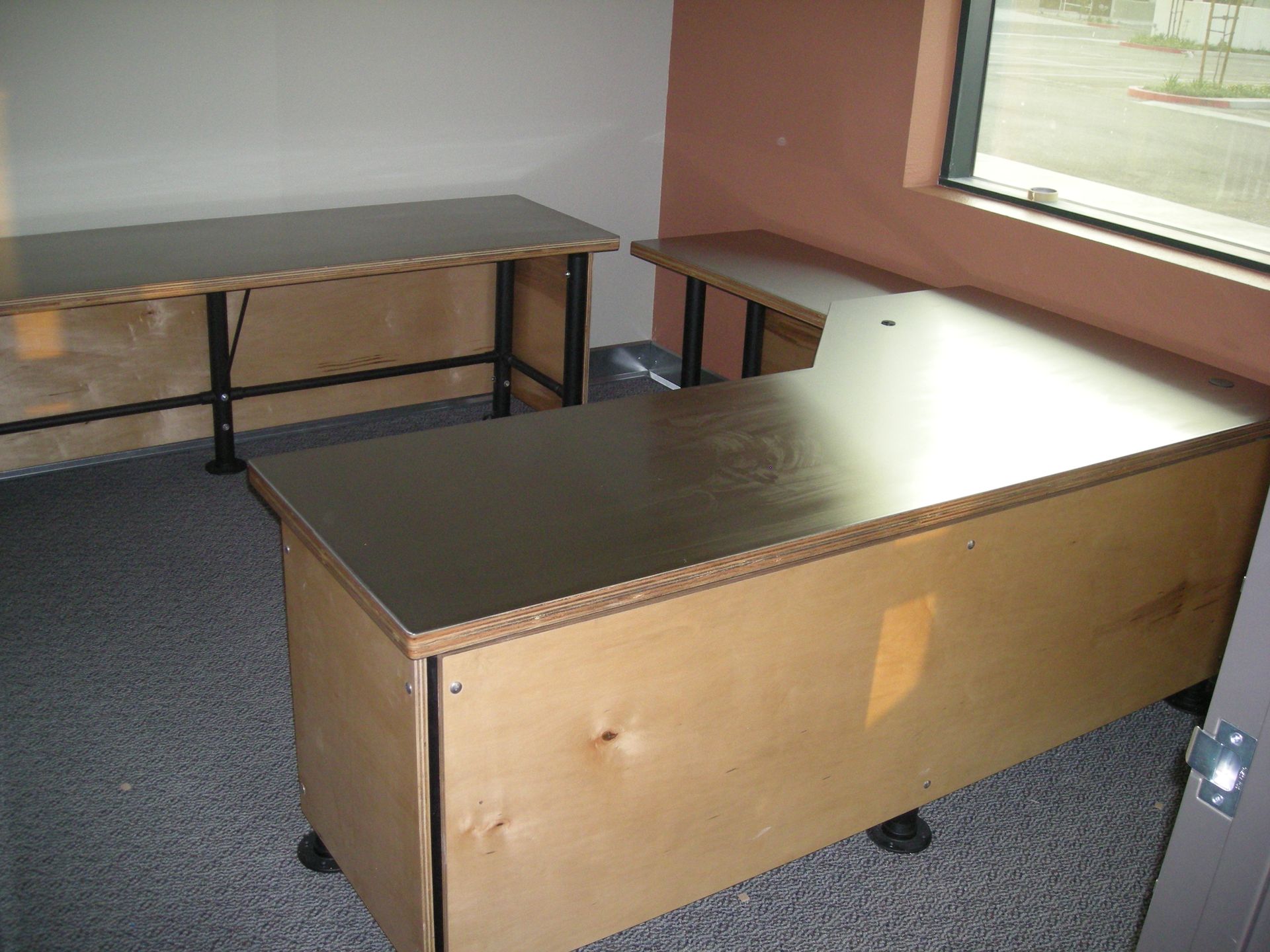 Two office desks in a room with a window, carpet, and light tan walls.