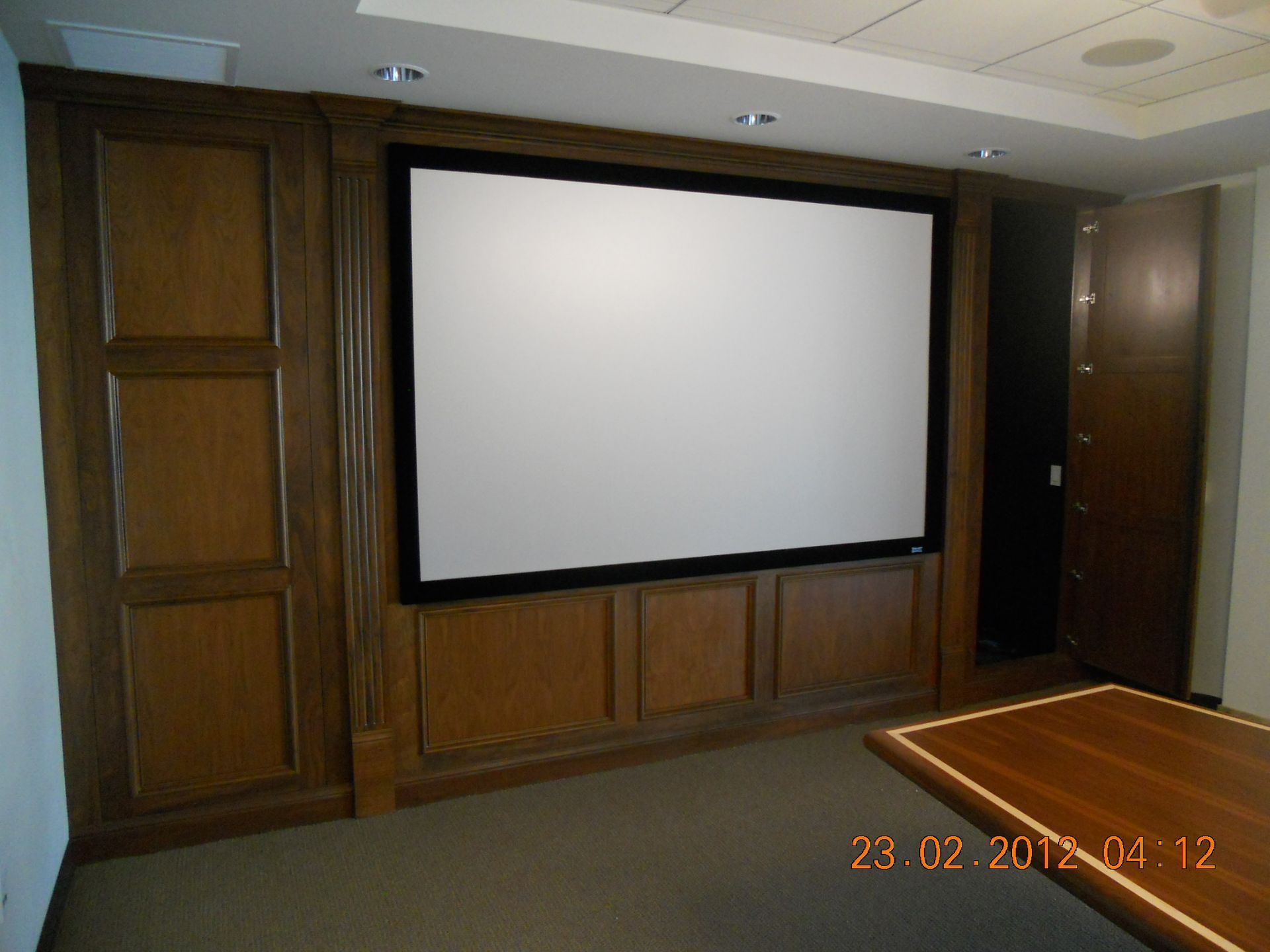 Wooden paneling with a large white projection screen in a room.