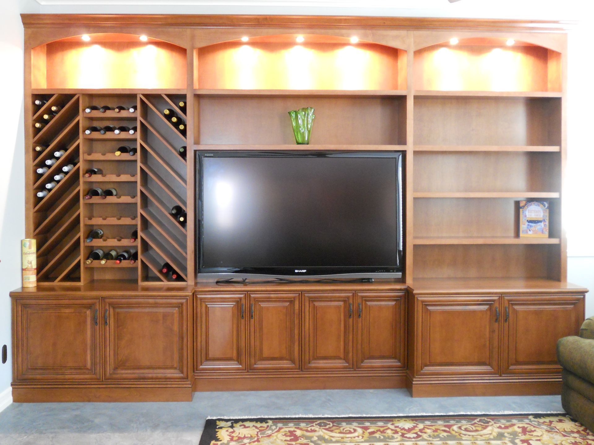 Built-in wooden entertainment center with wine storage, TV, and shelves.  Warm-toned wood, recessed lighting.