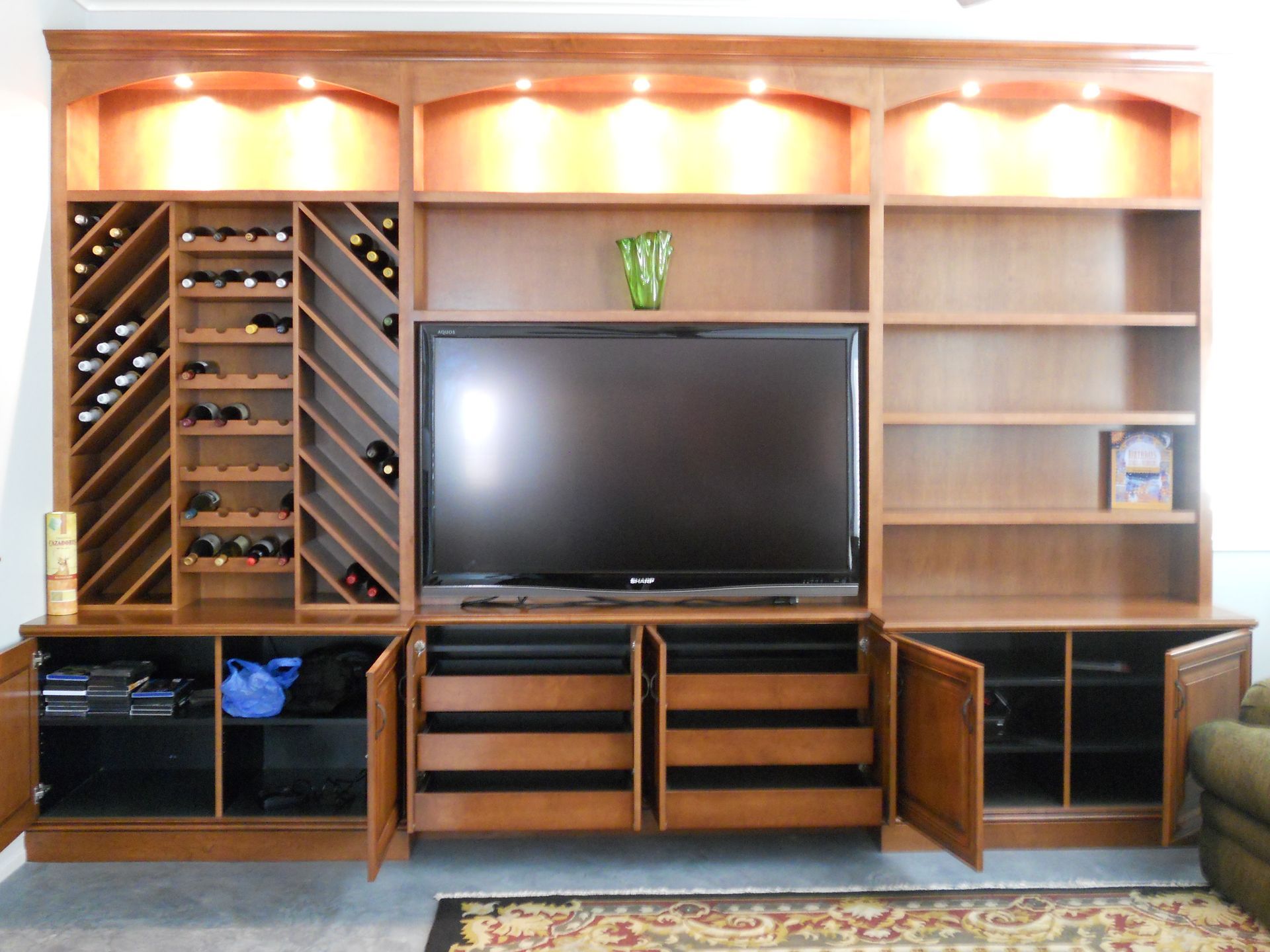 Built-in wooden entertainment center with wine racks, TV, shelves, and cabinets; lit with warm lights.