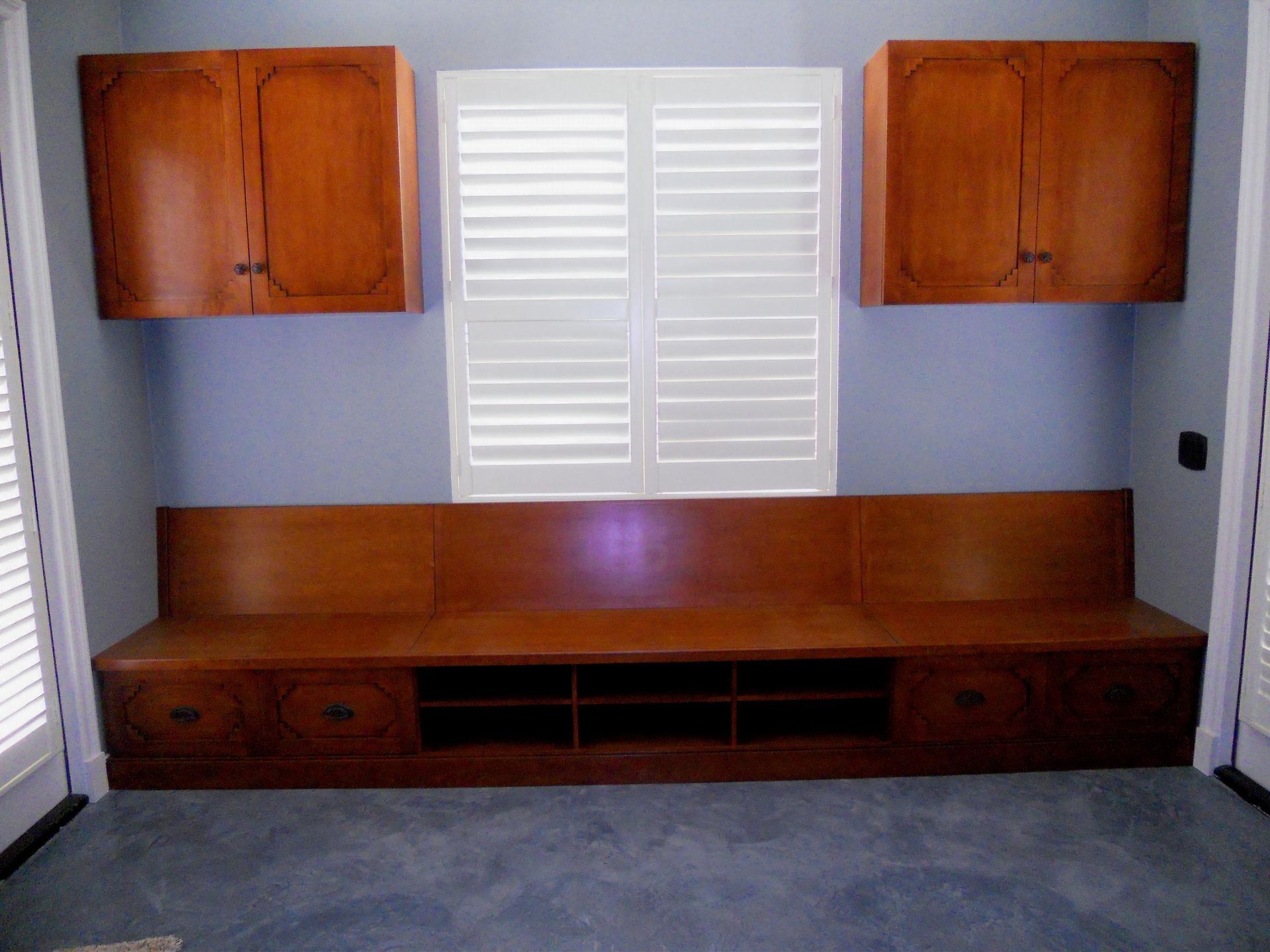 Built-in wooden bench with cabinets and window with shutters; blue walls and blue carpet.