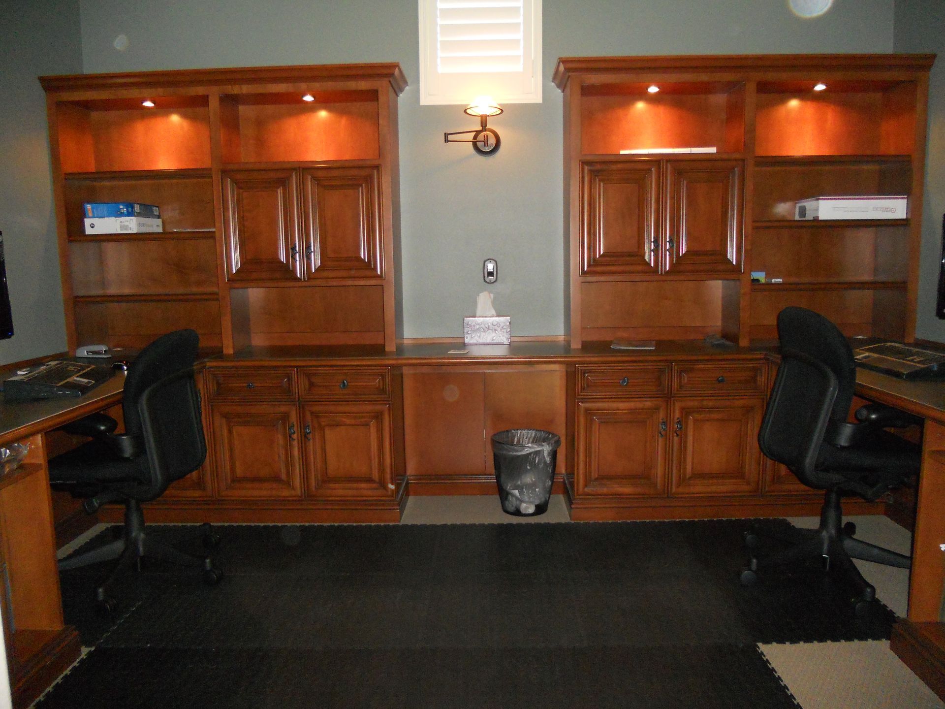 Two wooden desk stations with built-in bookshelves, chairs, and a wastebasket; a small window is overhead.