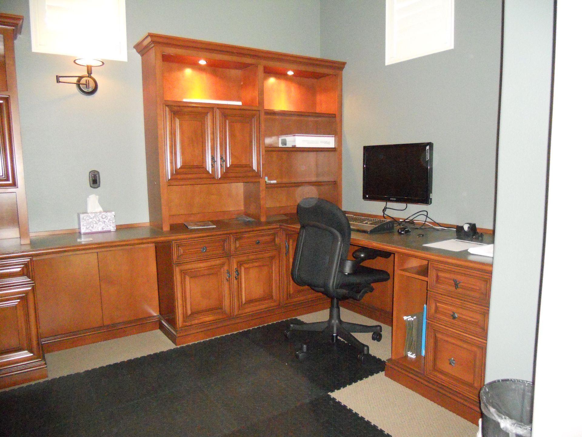 Office space with a large wooden desk and built-in shelving, computer monitor, and black chair.