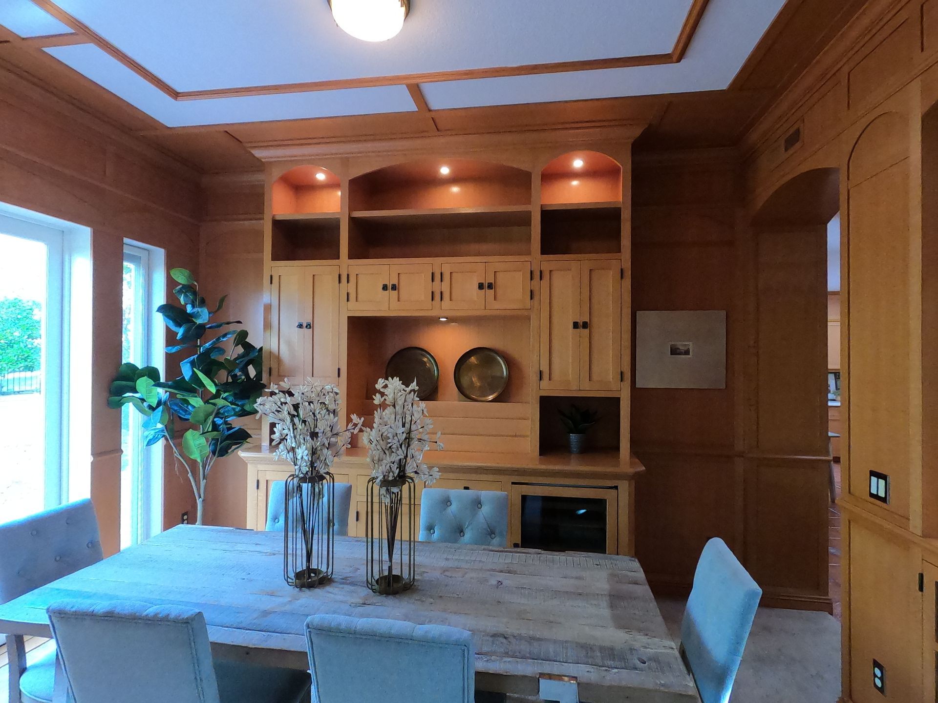 Dining room with wooden built-ins, table, and chairs. Decorative vases and a plant add color.