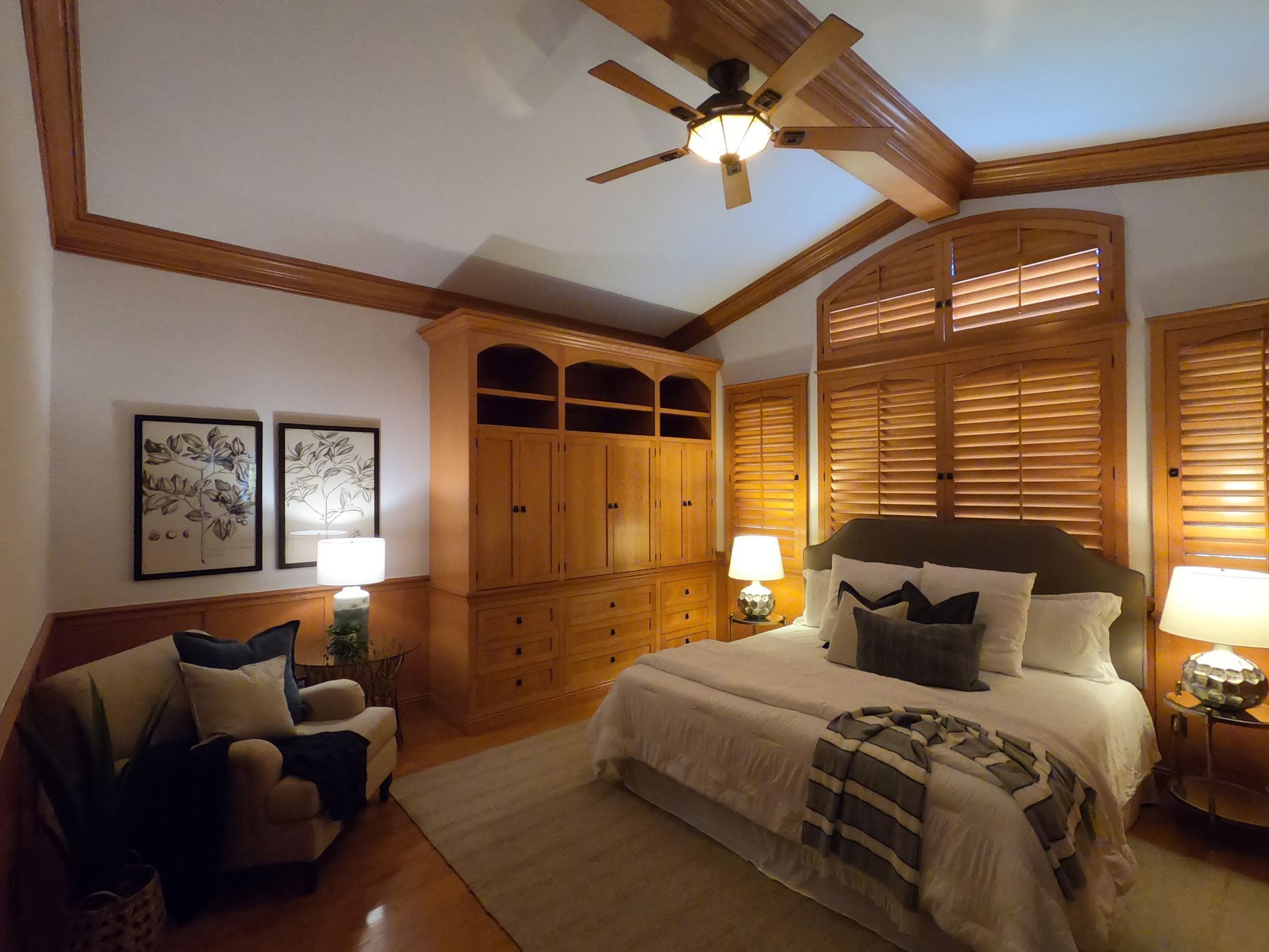 Bedroom with wooden ceiling beams, a large wardrobe, bed, armchair, and lamps.