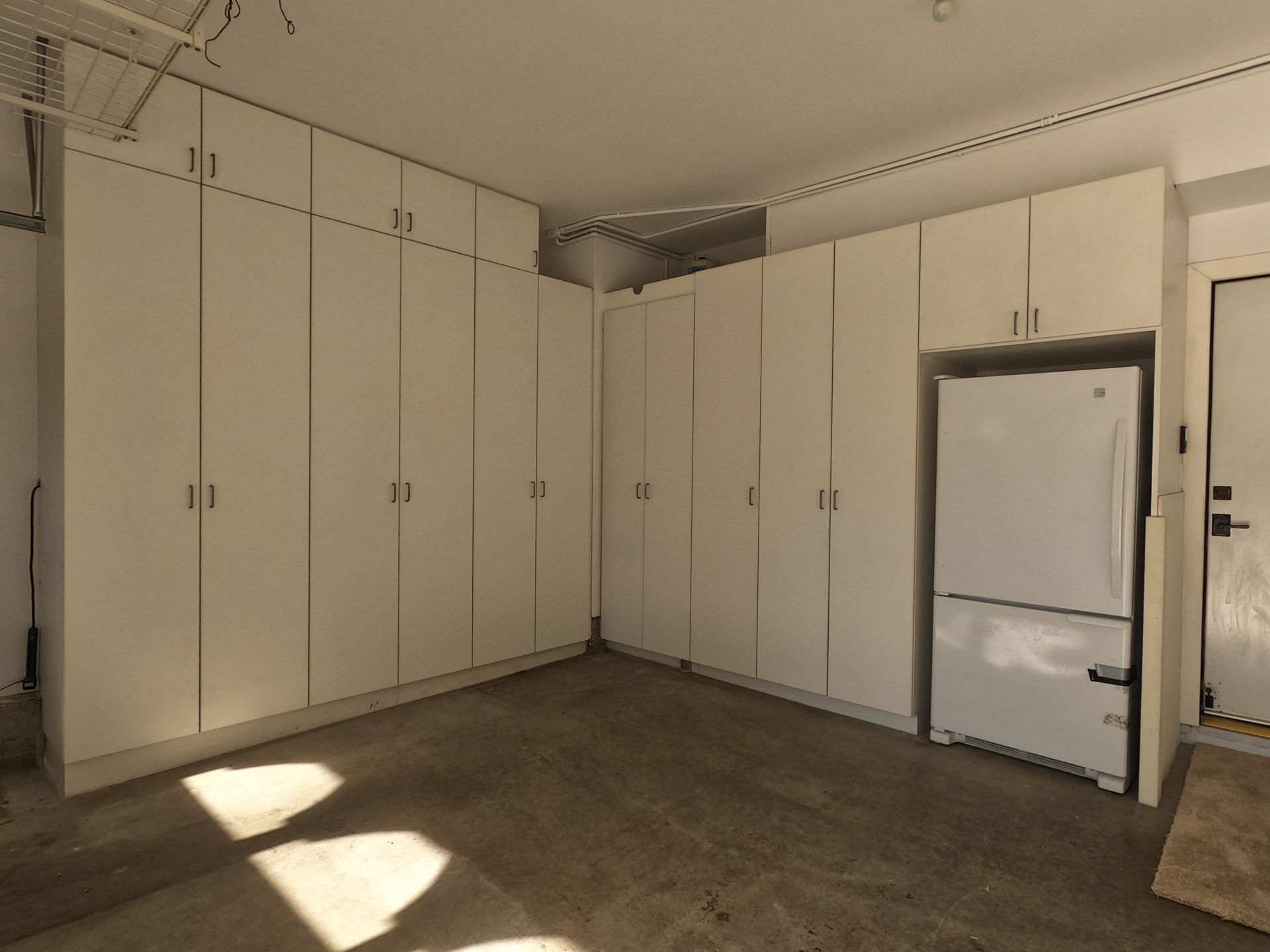 Garage interior with white cabinets and refrigerator. Concrete floor.
