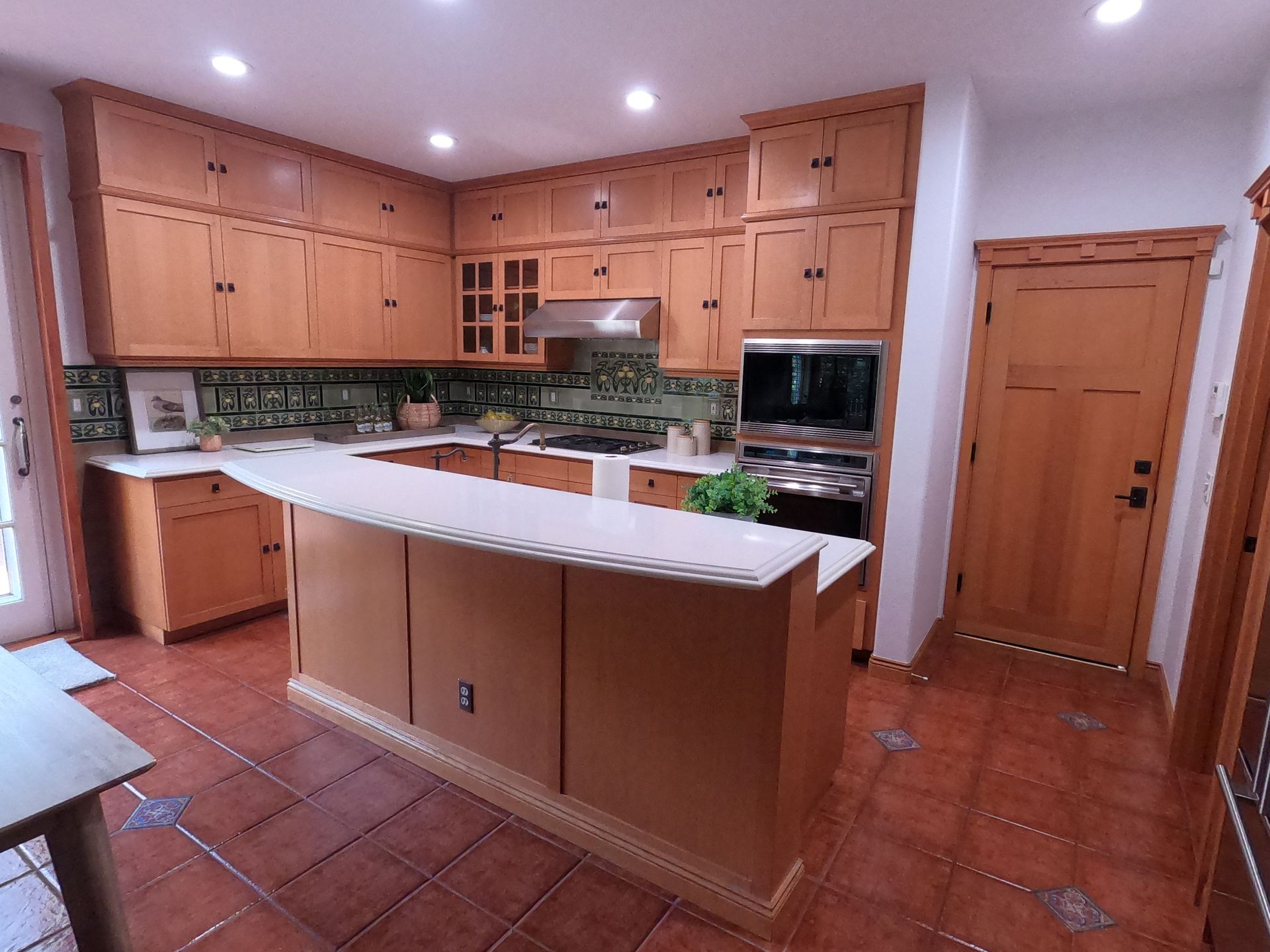 Kitchen with light wood cabinets, white countertops, and terracotta tile floor.
