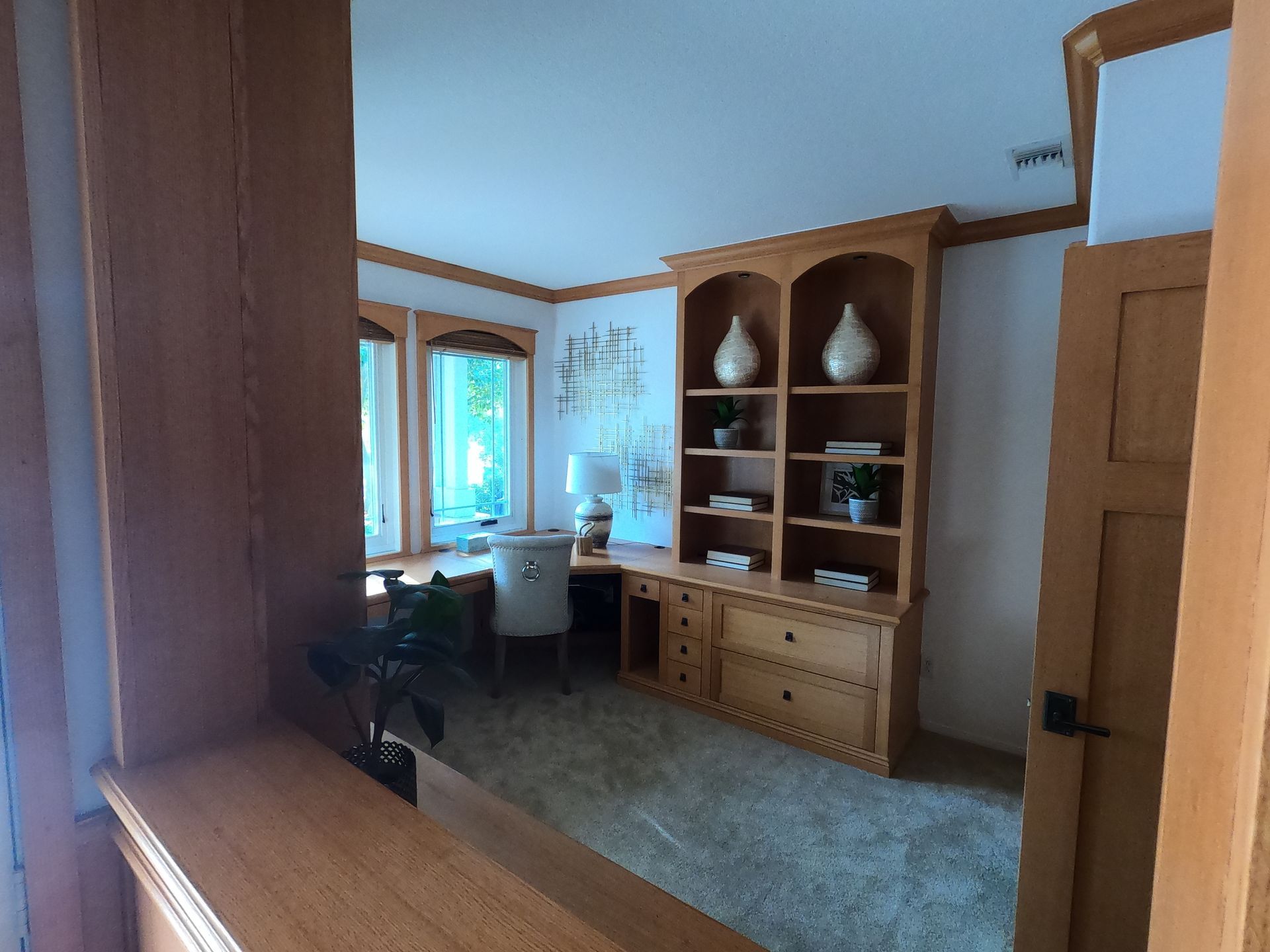 Wooden desk and bookshelf in a room with a window, carpet, and light-colored walls.