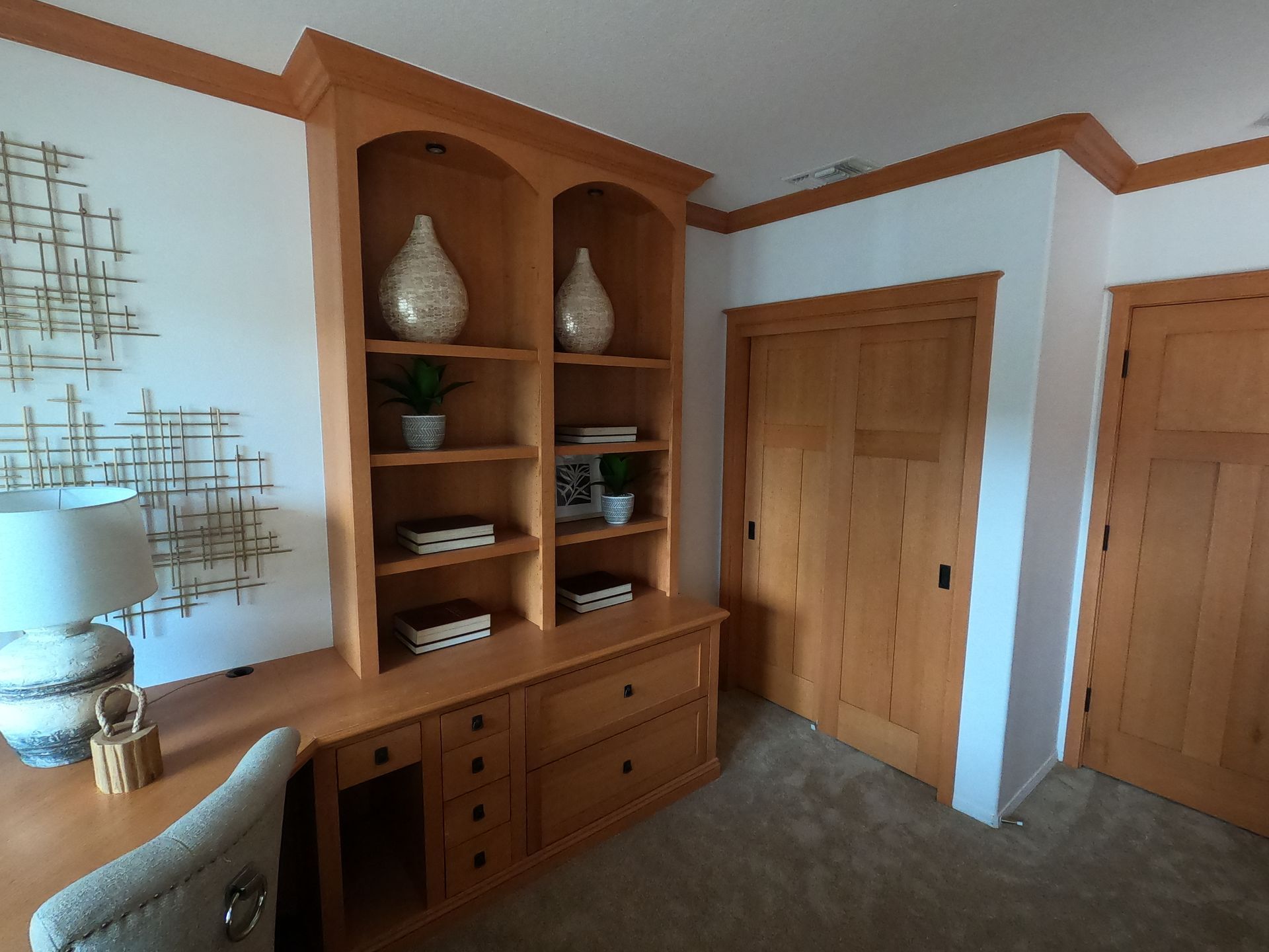 Wooden built-in shelving and desk in a room with a closed door. Beige walls, carpet and crown molding.