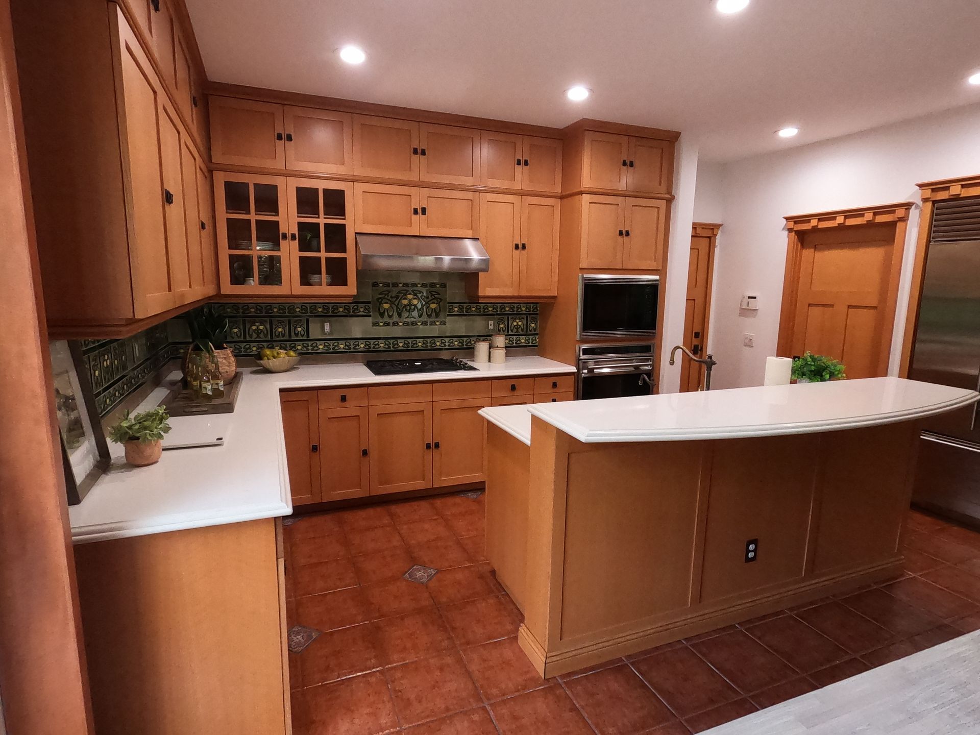 Kitchen with wooden cabinets, white countertops, stainless steel appliances, and brown tile flooring.