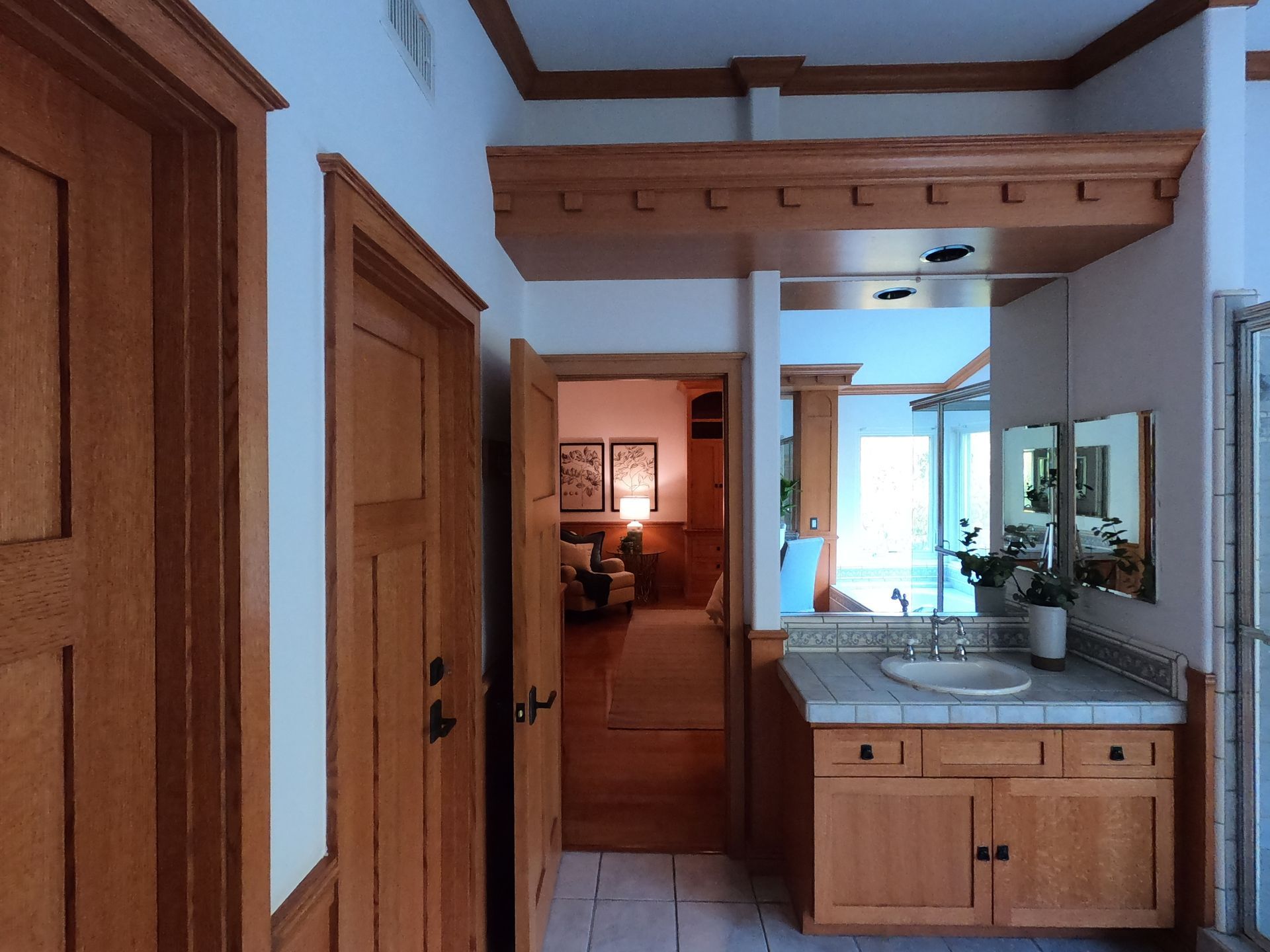 Hallway with wooden doors, a vanity, and a glimpse into a room with furniture and artwork.