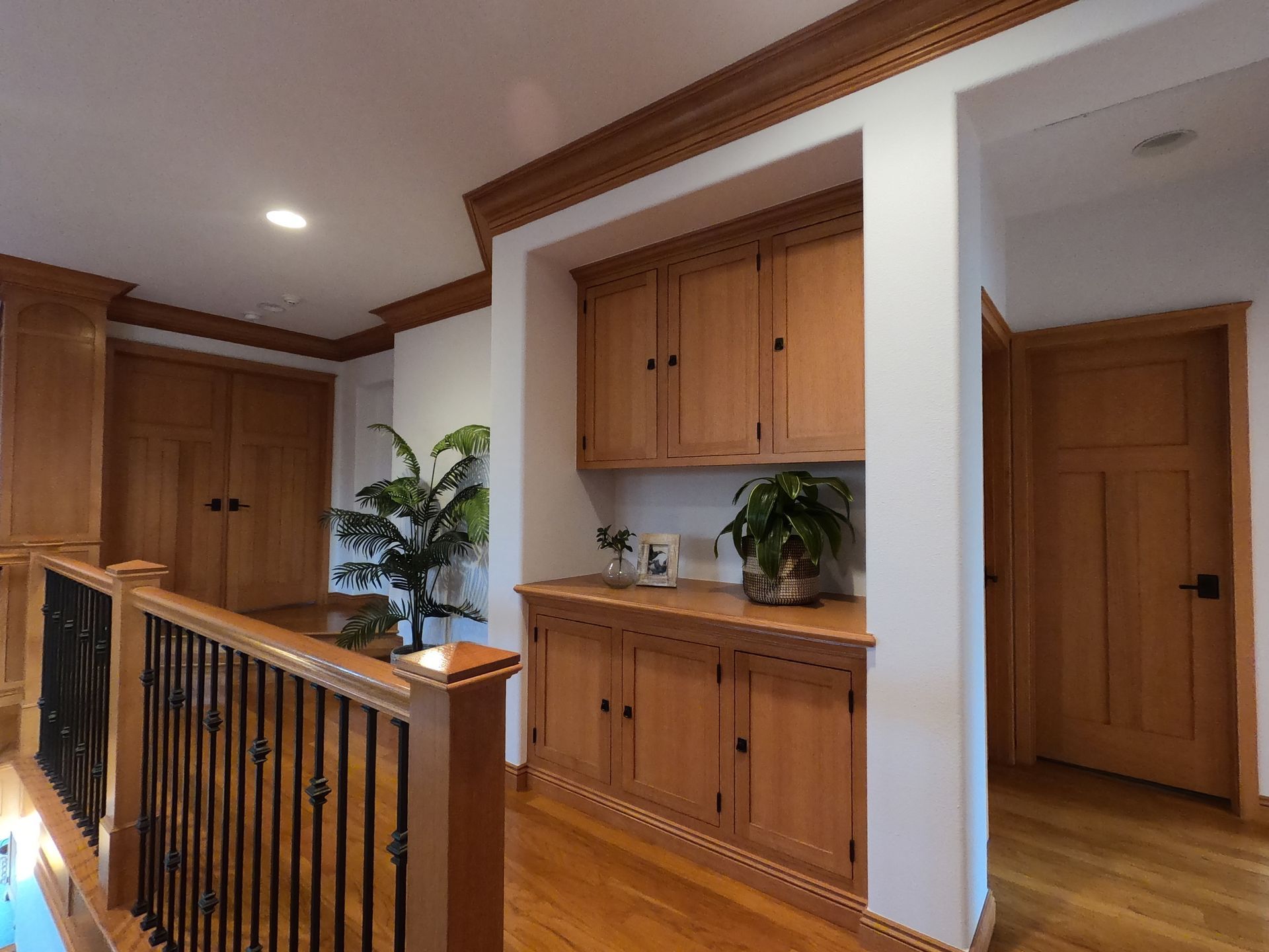 Hallway with wooden cabinets, doors, and a staircase. Hardwood floors and trim.