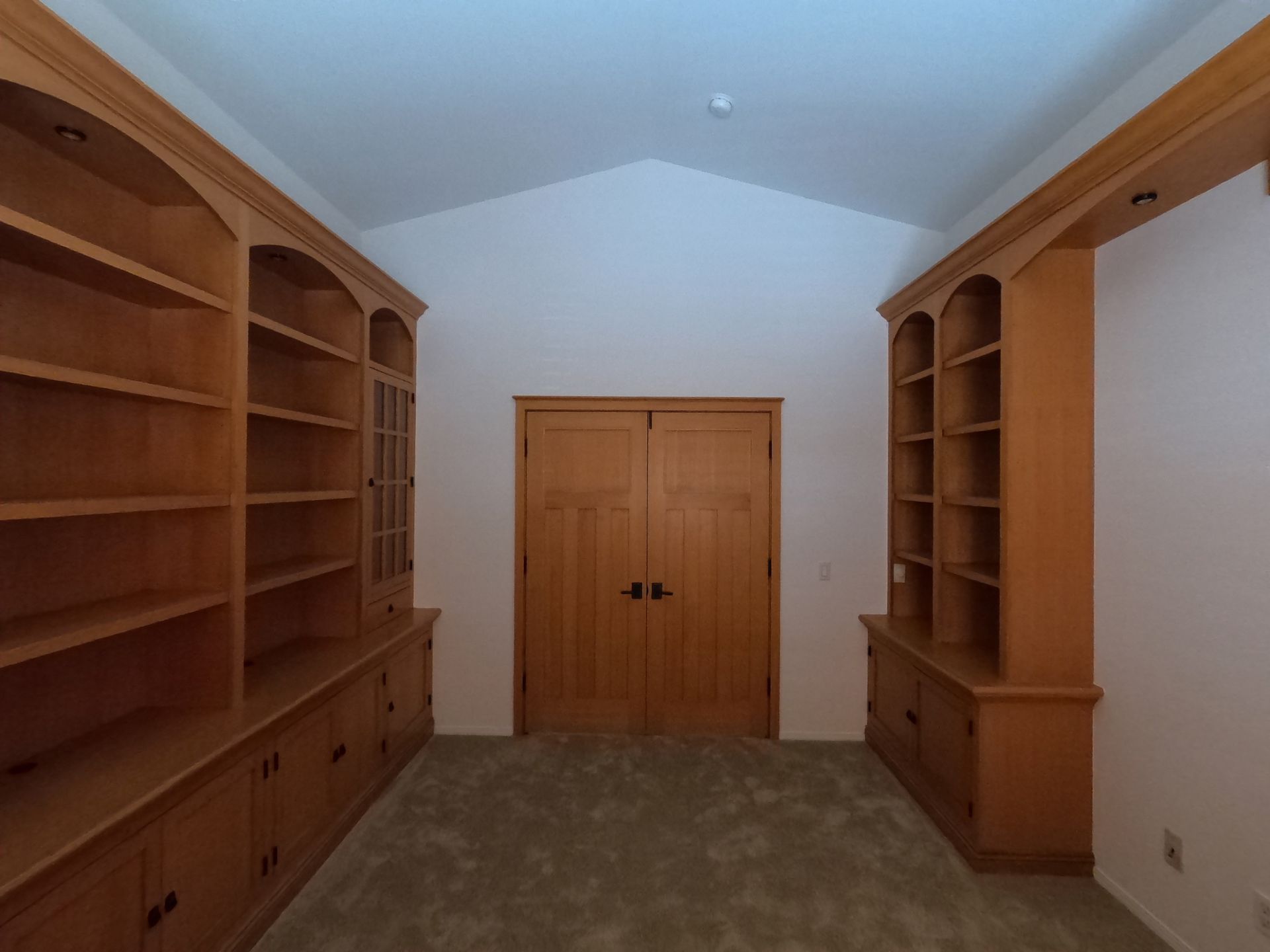 Wooden built-in bookshelves frame a double-door entry. Light brown wood, beige carpet, and a white ceiling.