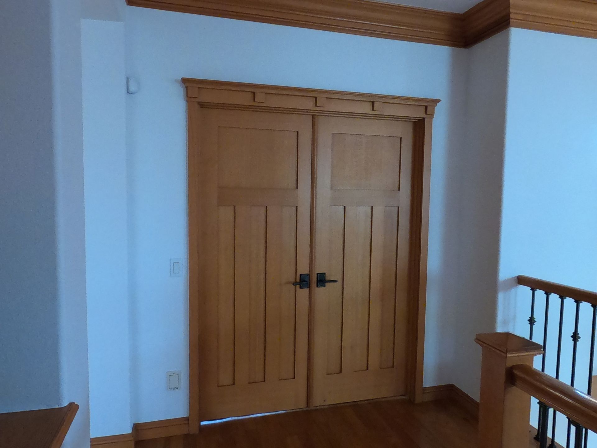 Double wooden doors with dark hardware, framed by light-colored wood trim and white walls.