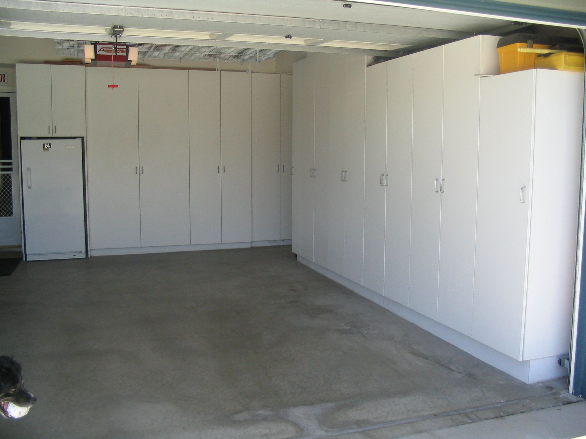 Garage interior with white cabinets and a refrigerator. Concrete floor.