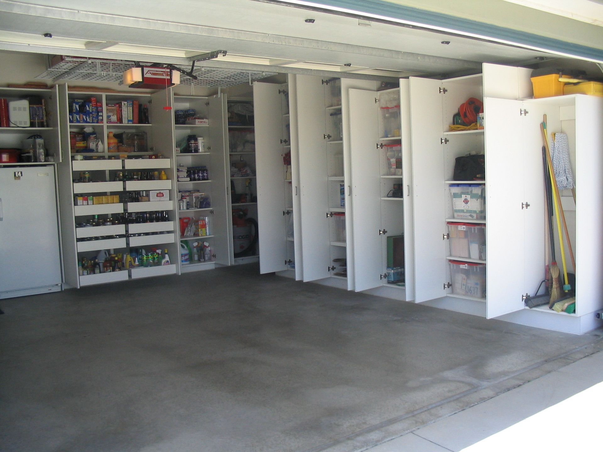 Garage interior with built-in white cabinets filled with various items for storage.