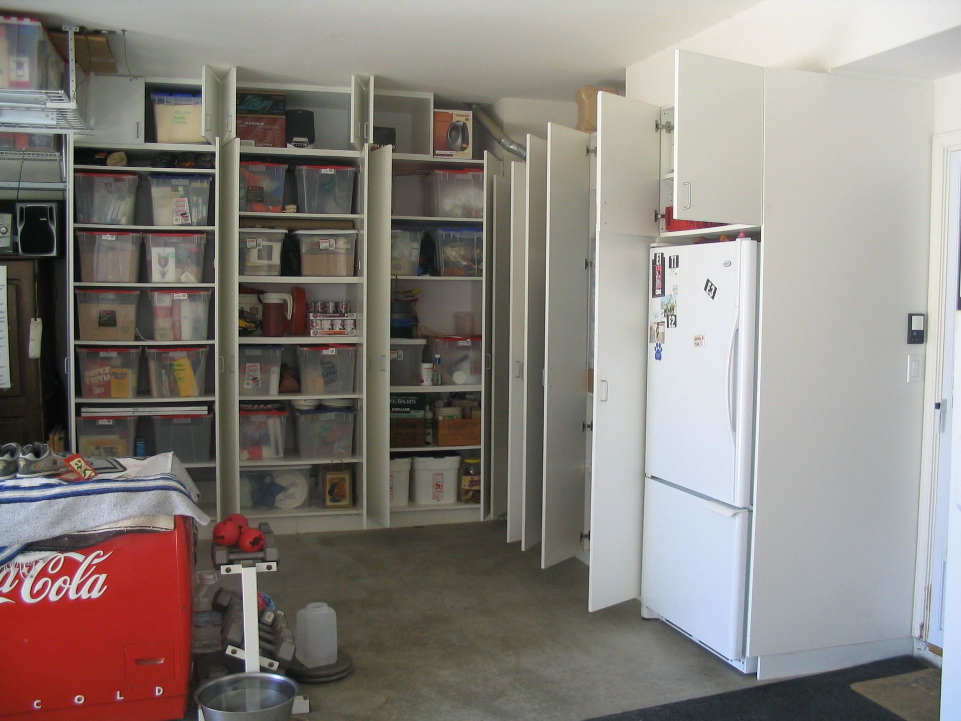 Garage interior with shelving units, refrigerator, and vintage Coca-Cola cooler.