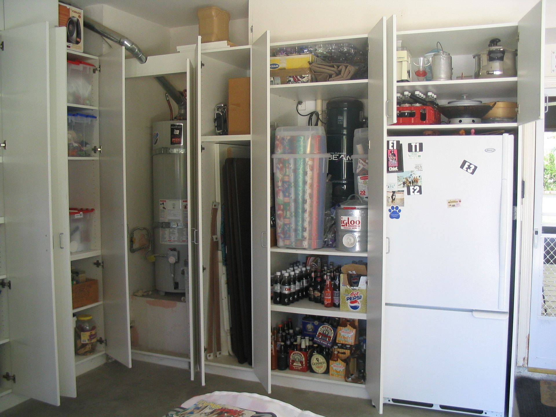 Garage storage cabinets, white, with doors open, displaying various items including appliances, tools, and food.