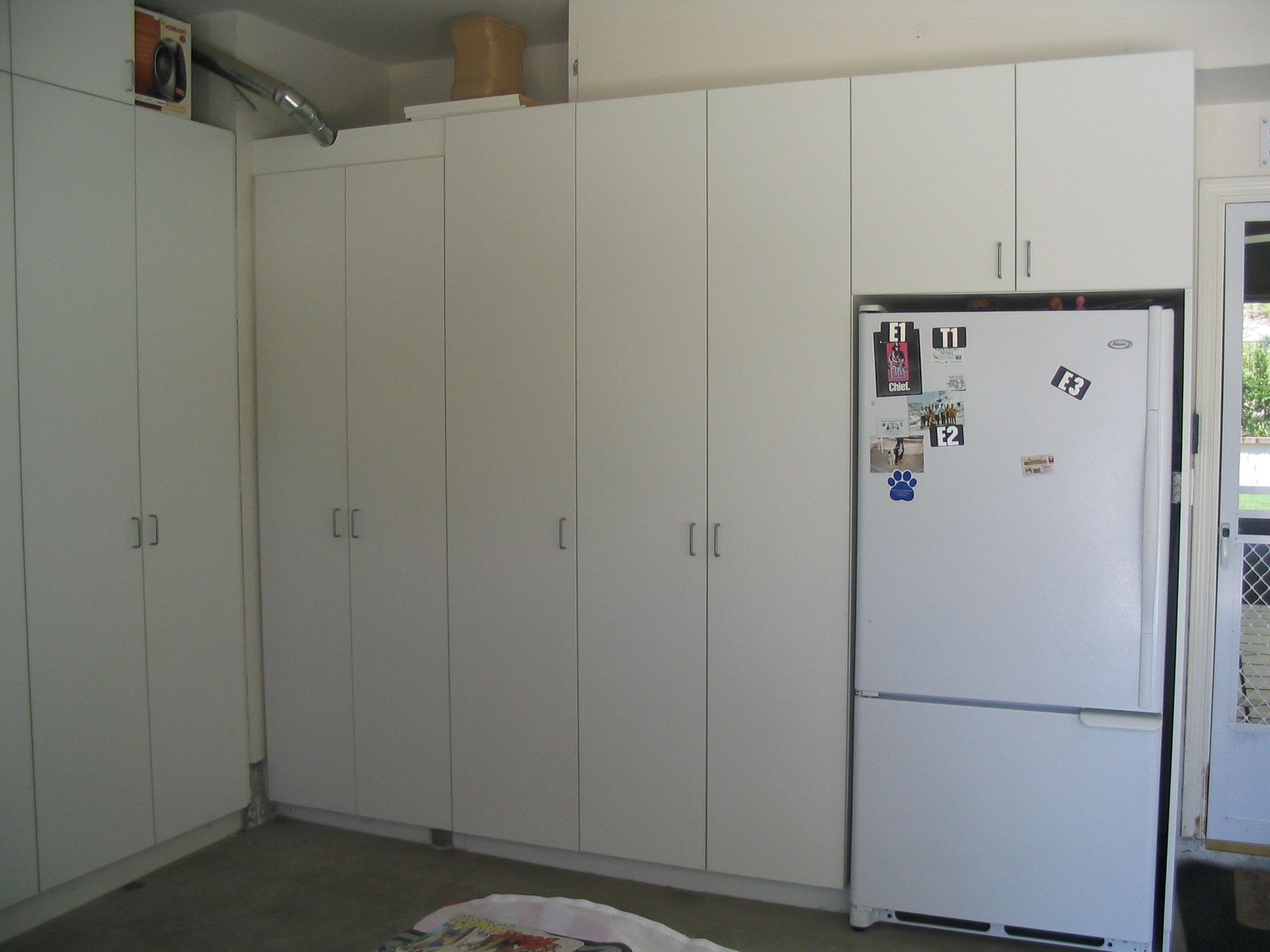 White storage cabinets and a refrigerator in a garage.