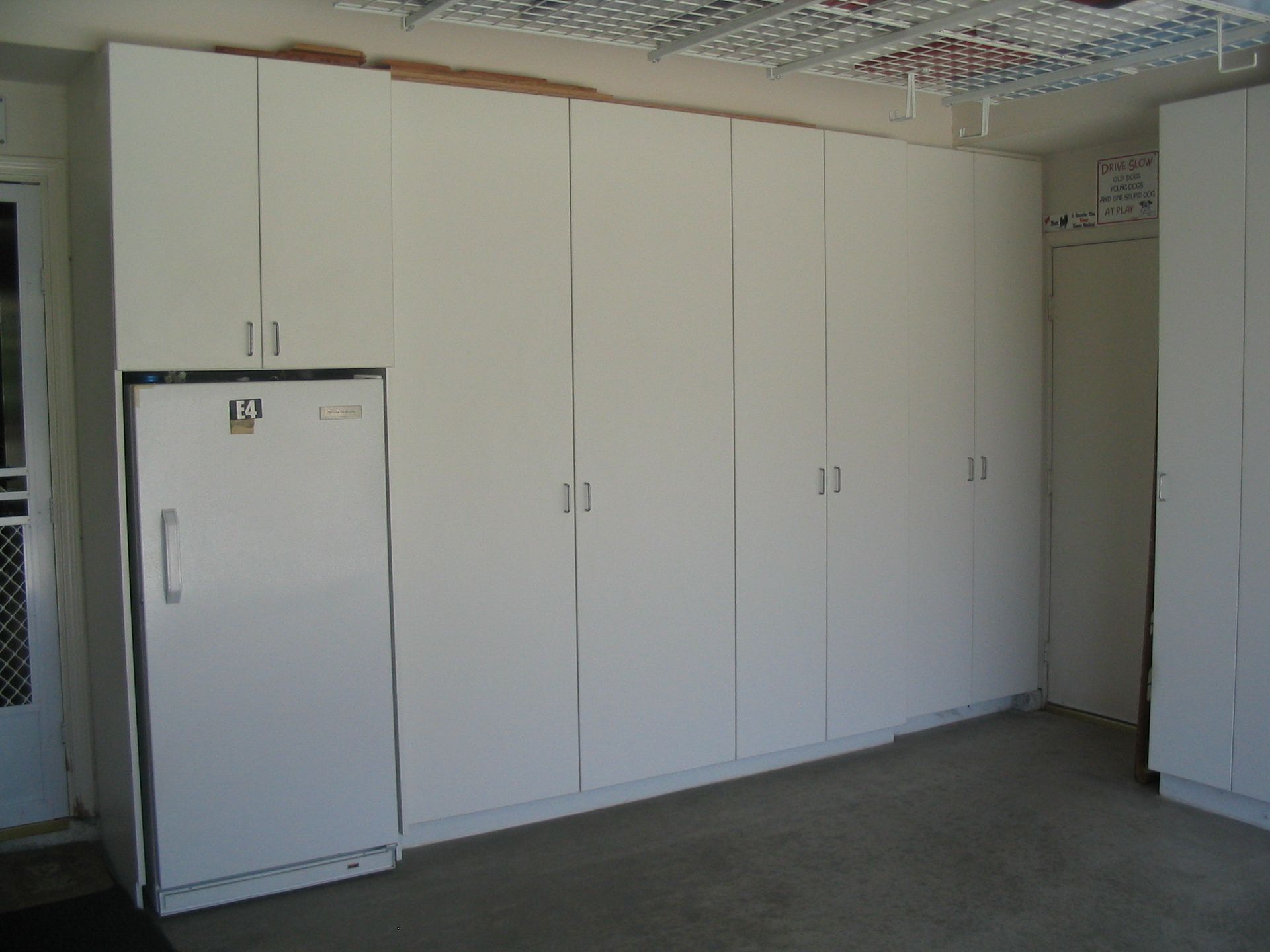 White cabinets and a refrigerator line a garage wall.