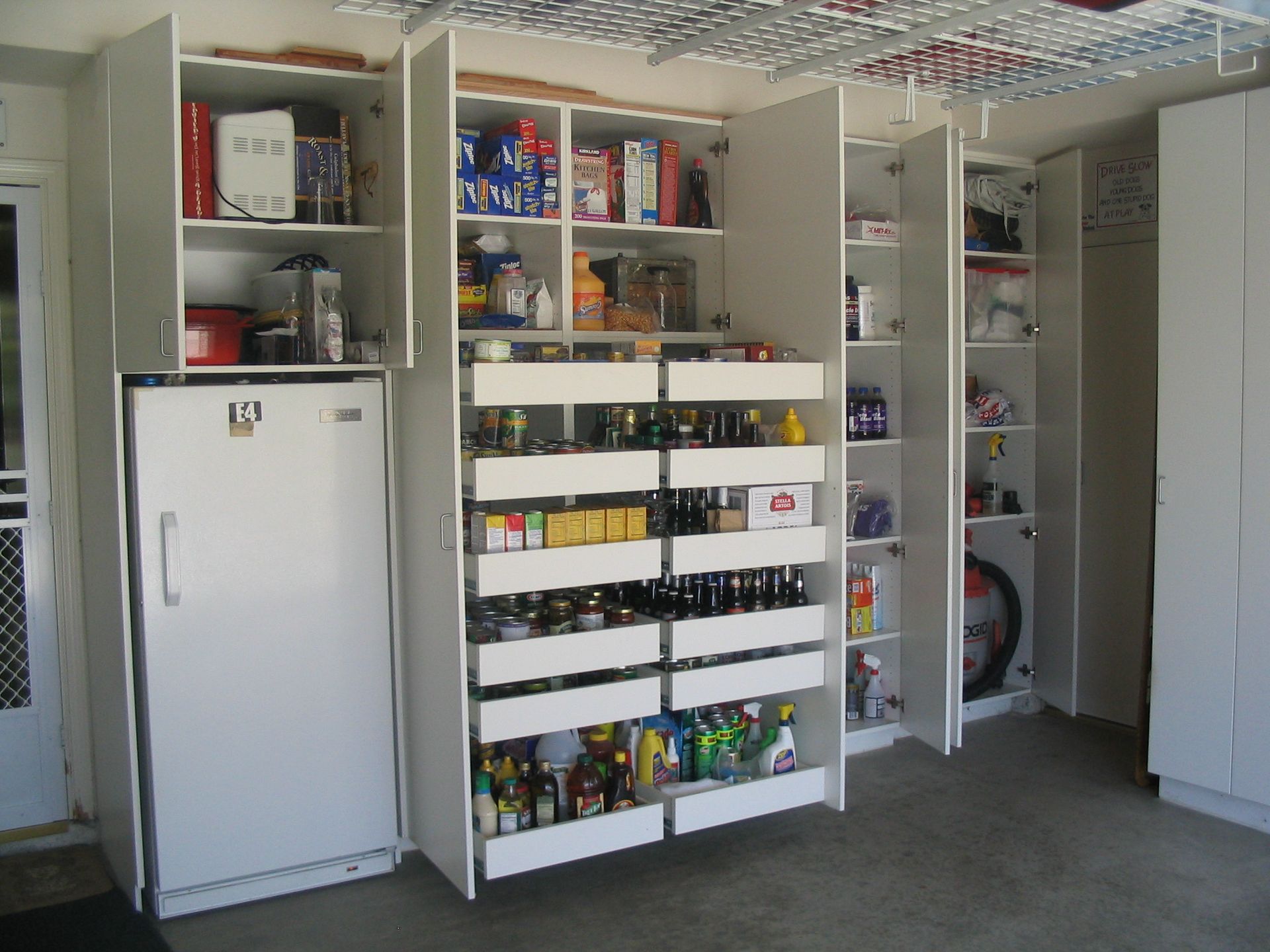 White garage storage cabinets and a refrigerator. One open cabinet with drawers.