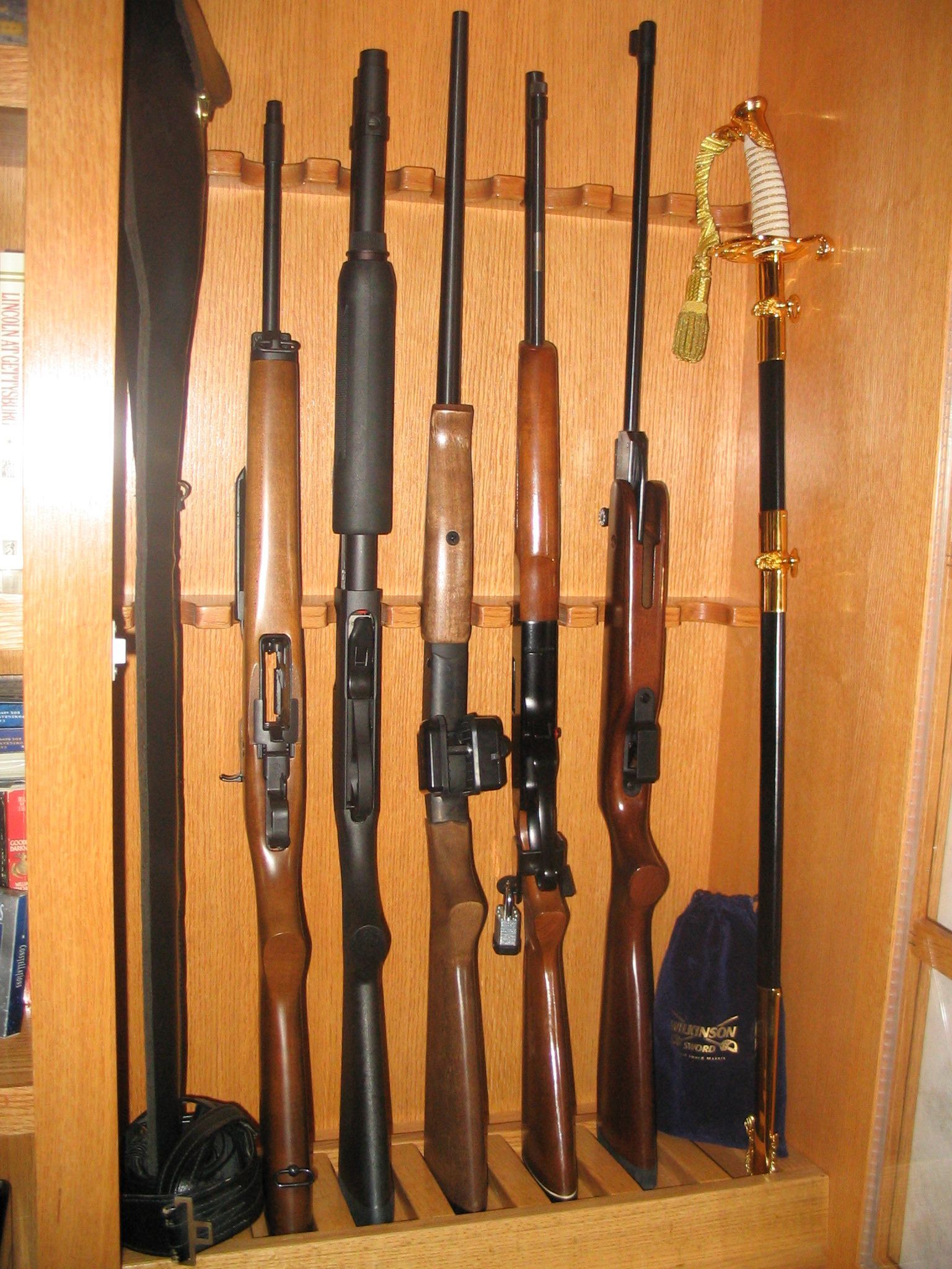 Guns in a wooden cabinet, with varying barrel lengths and a decorative sword-like object.