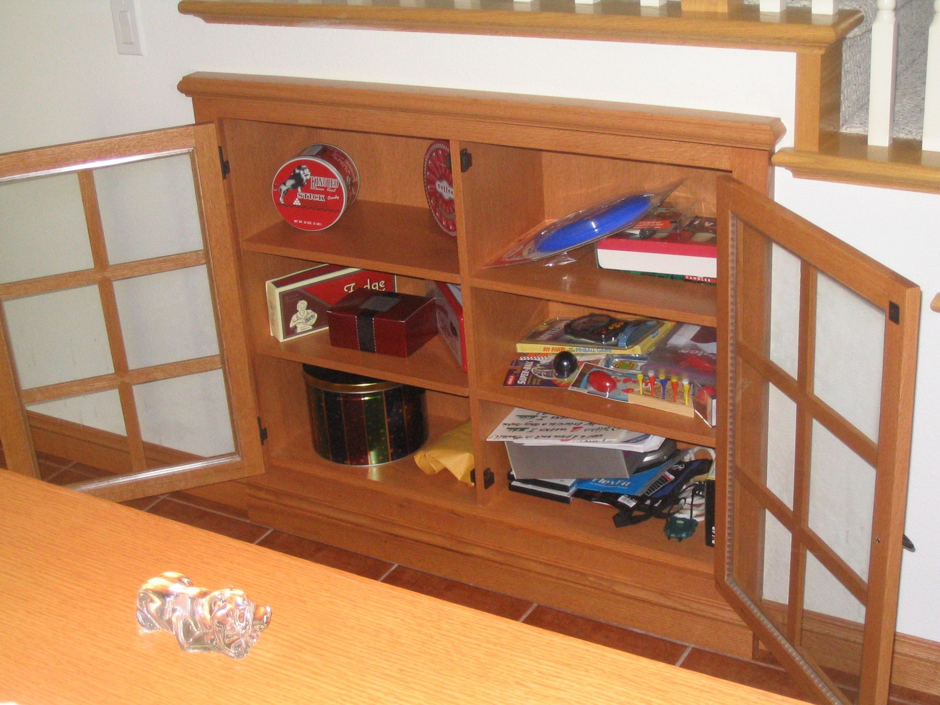 Wooden cabinet with glass doors, open, filled with various objects, set on a wooden floor.