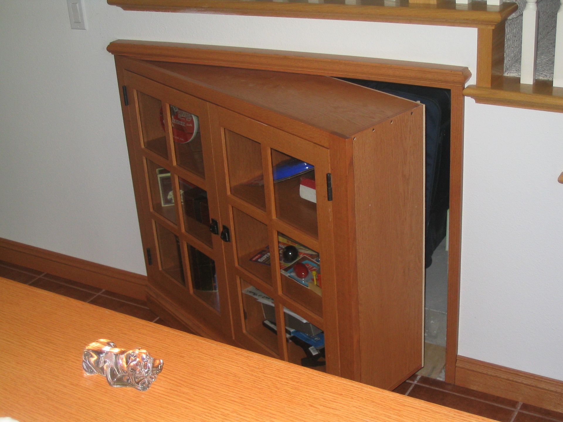 Wooden cabinet door concealing a secret doorway in a home. The cabinet is filled with items.