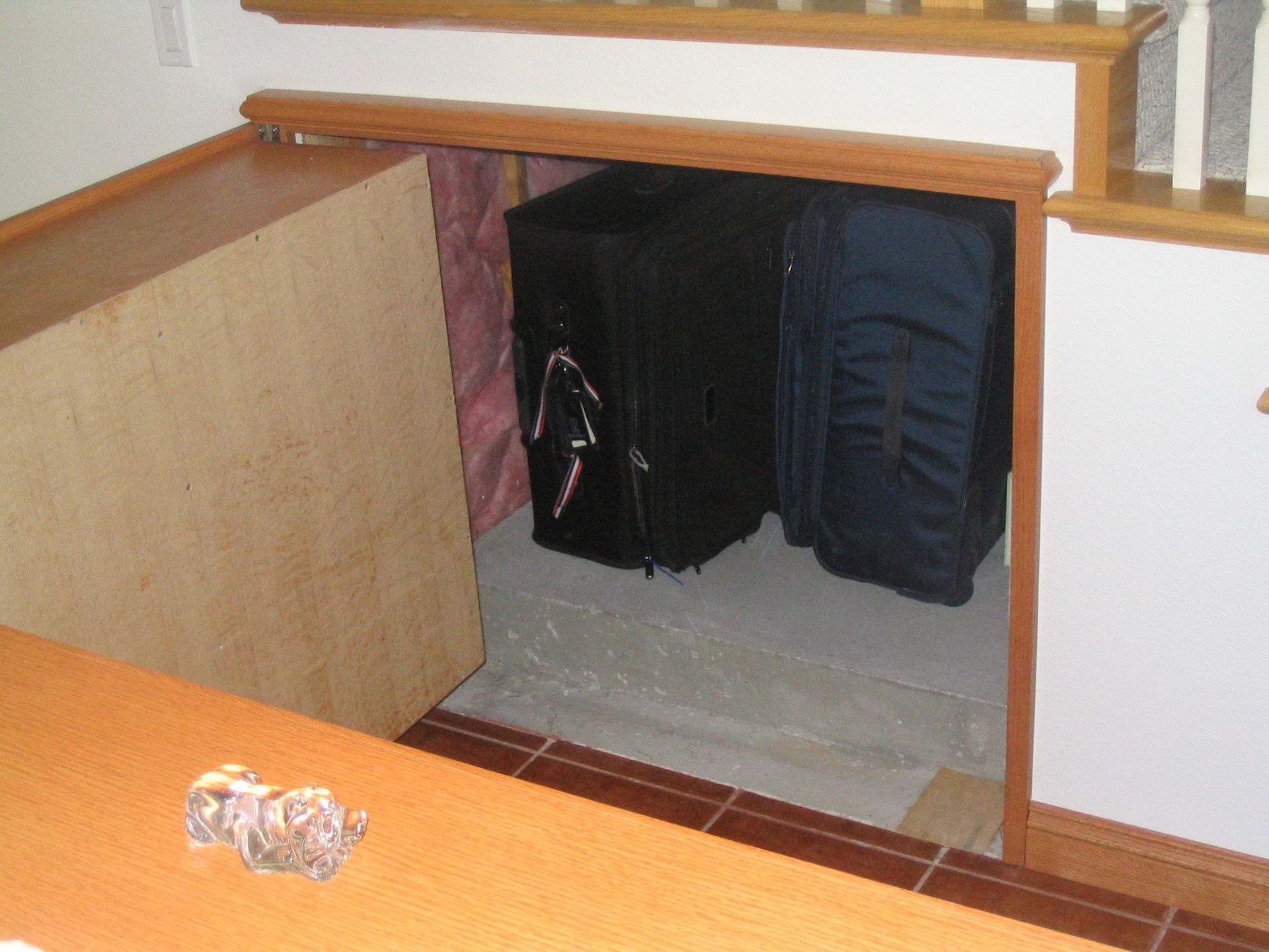 Storage closet under stairs with sliding wooden door, holding luggage.
