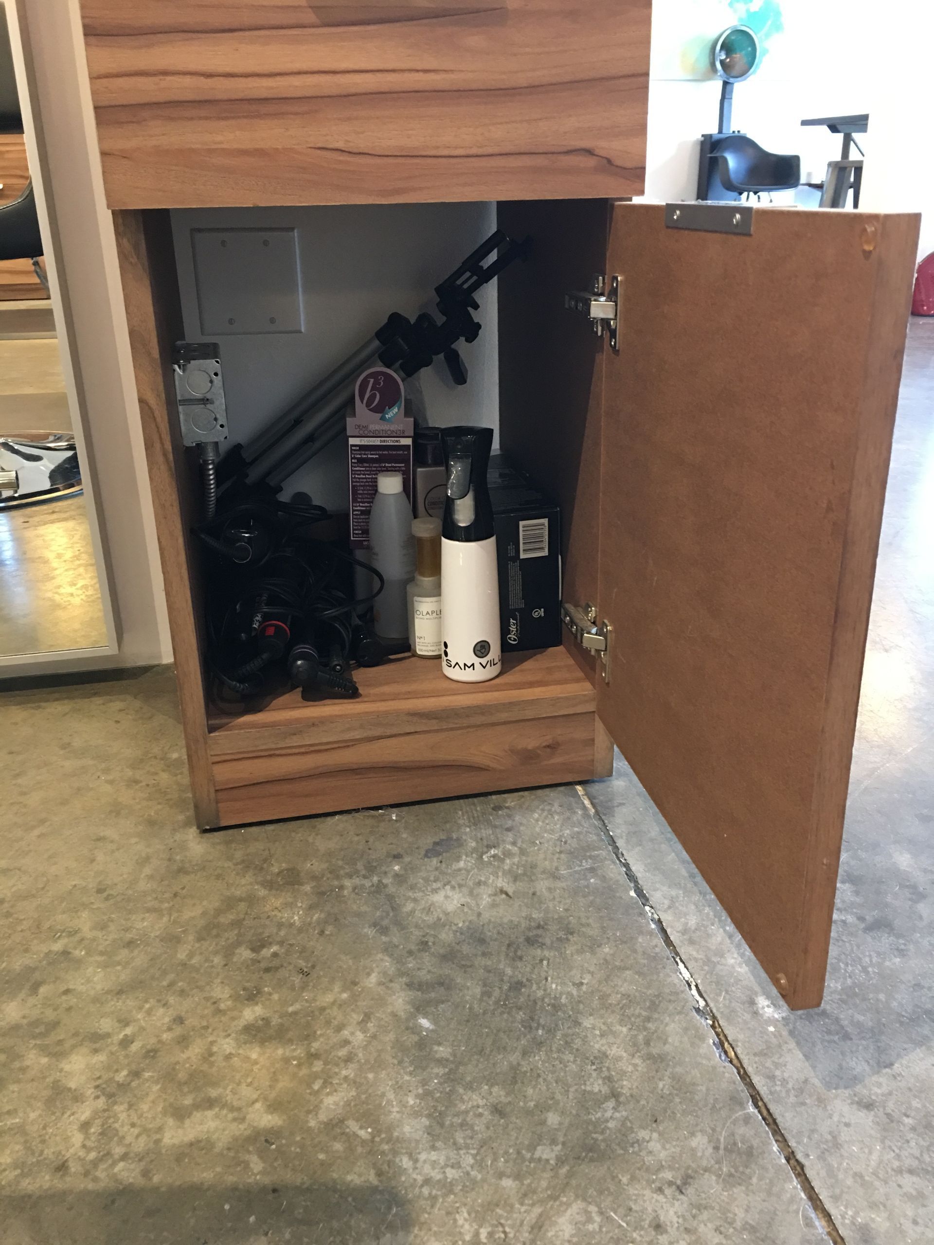 Open cabinet with various objects inside, including bottles and a tripod, on a concrete floor.
