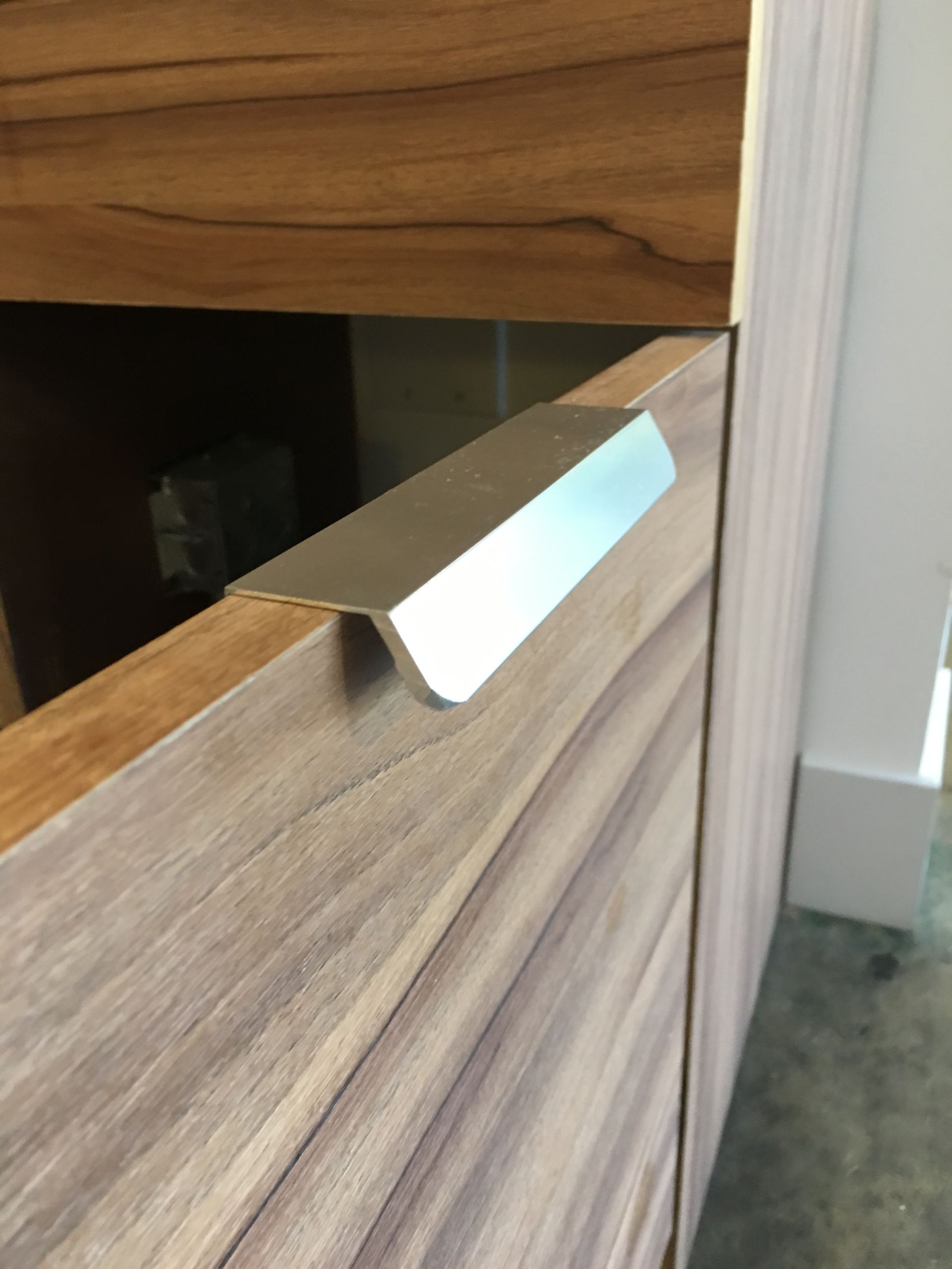 Silver cabinet pull on a light brown wooden cabinet.