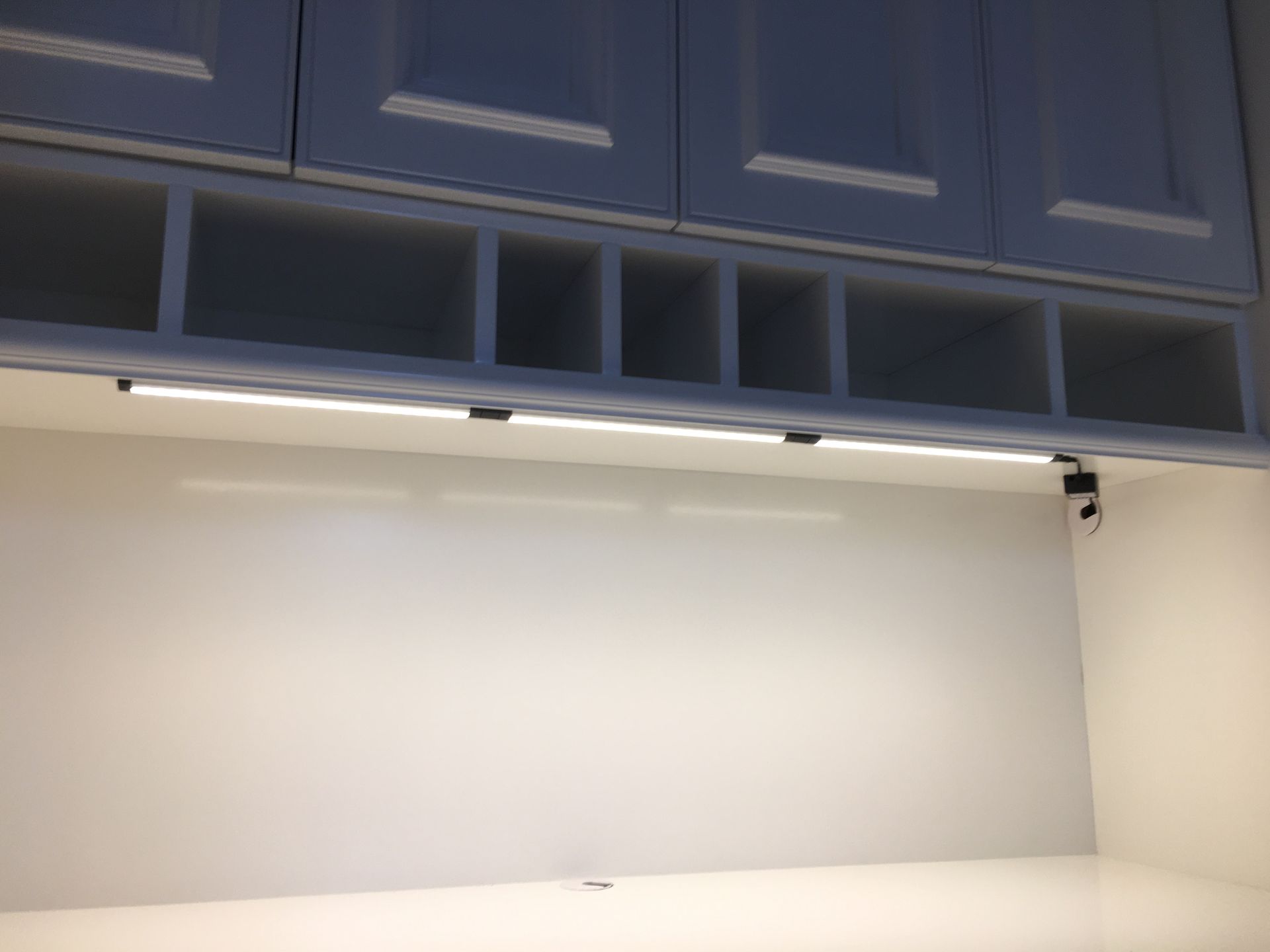 Kitchen cabinets with under-cabinet LED lights illuminating a white countertop and recessed cubbies above.