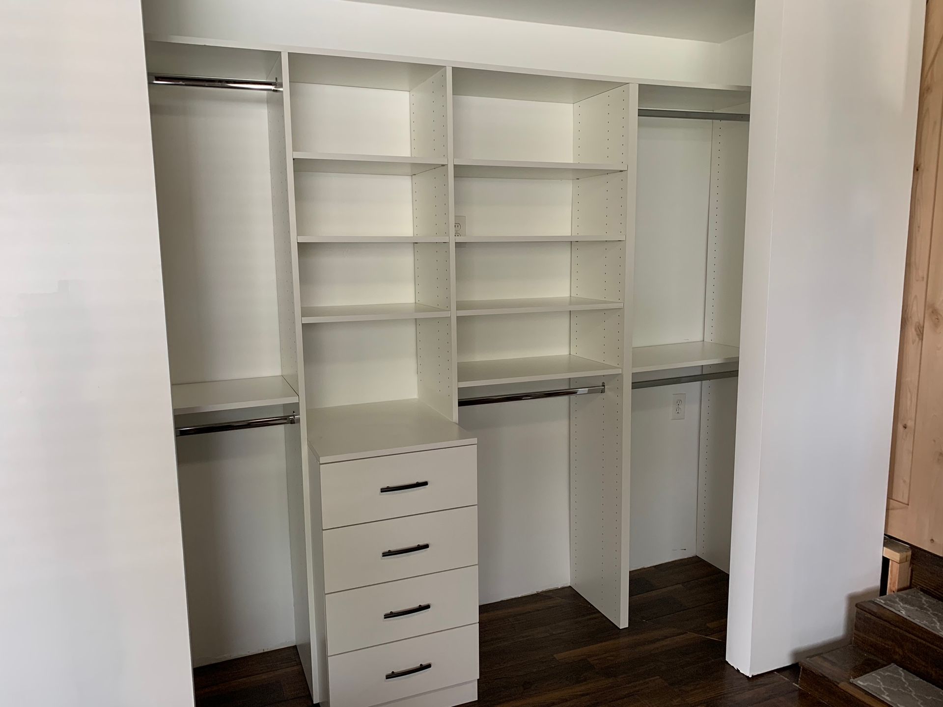 Empty white closet with shelves, drawers, and hanging rods. Brown wood floor.