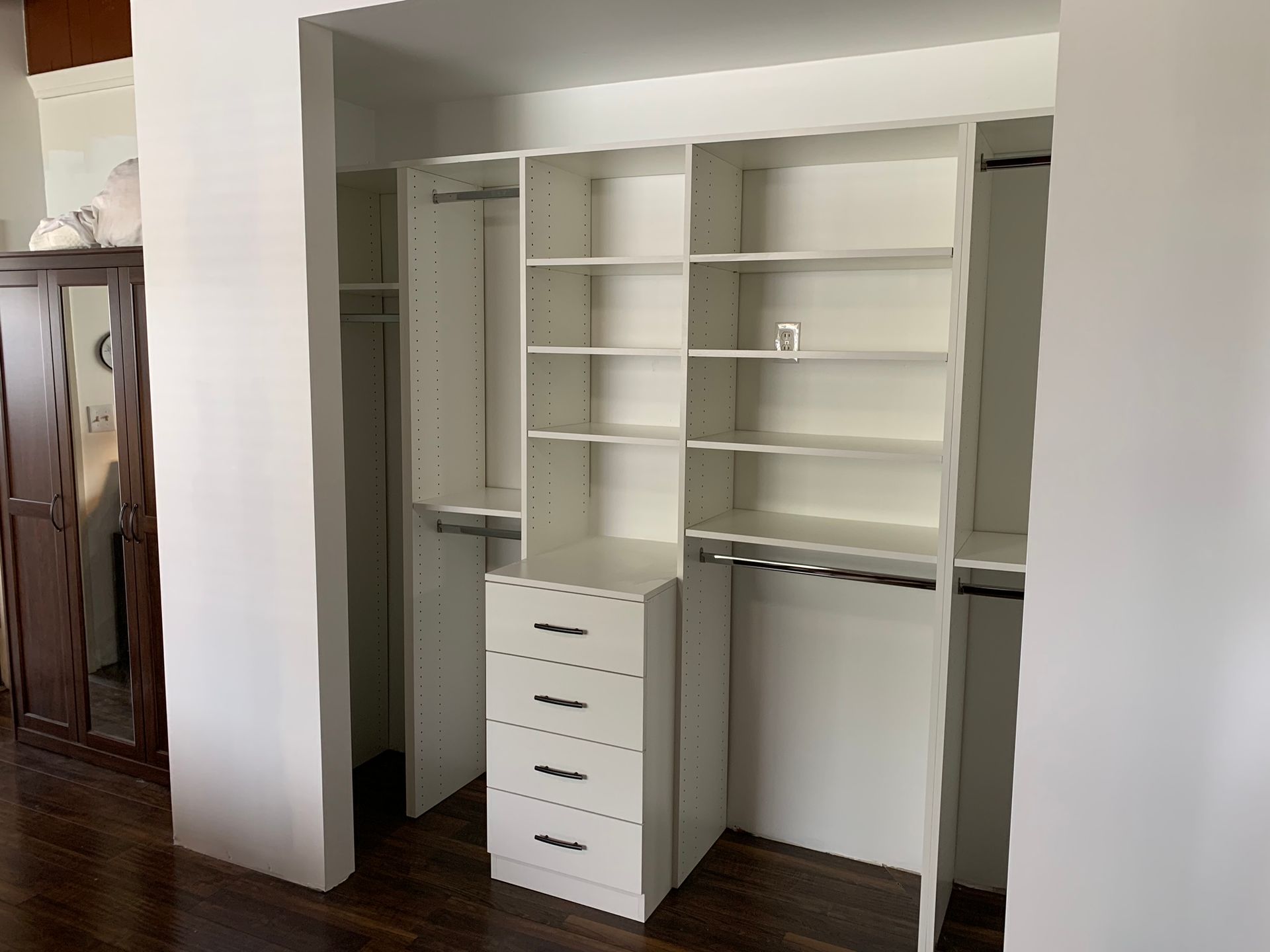 White closet organizer with drawers, shelves, and hanging rods. Dark wood floor.
