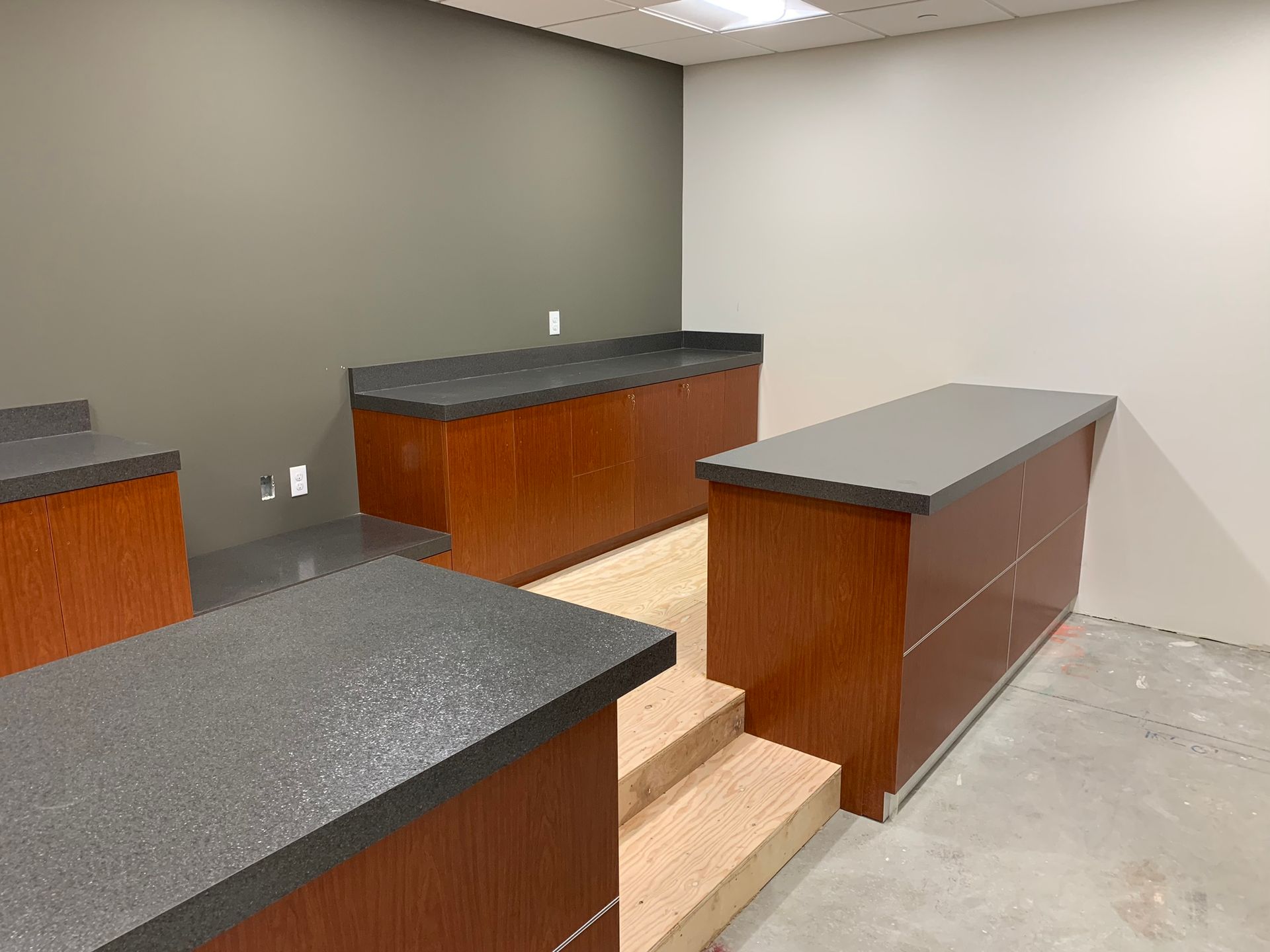 Empty room with wooden cabinets, gray countertops, and concrete floors. The walls are gray and white.