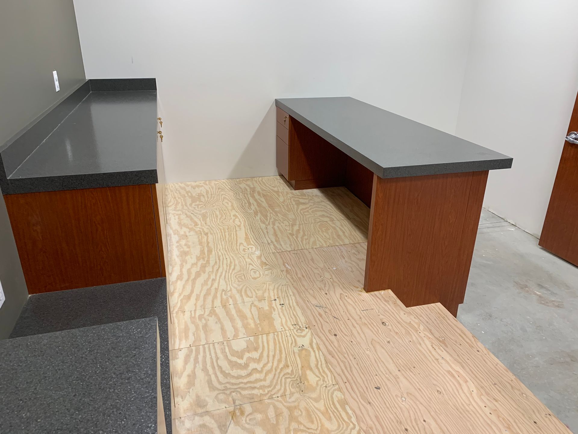 A room with two wooden counters, one long and one short, with a plywood floor.